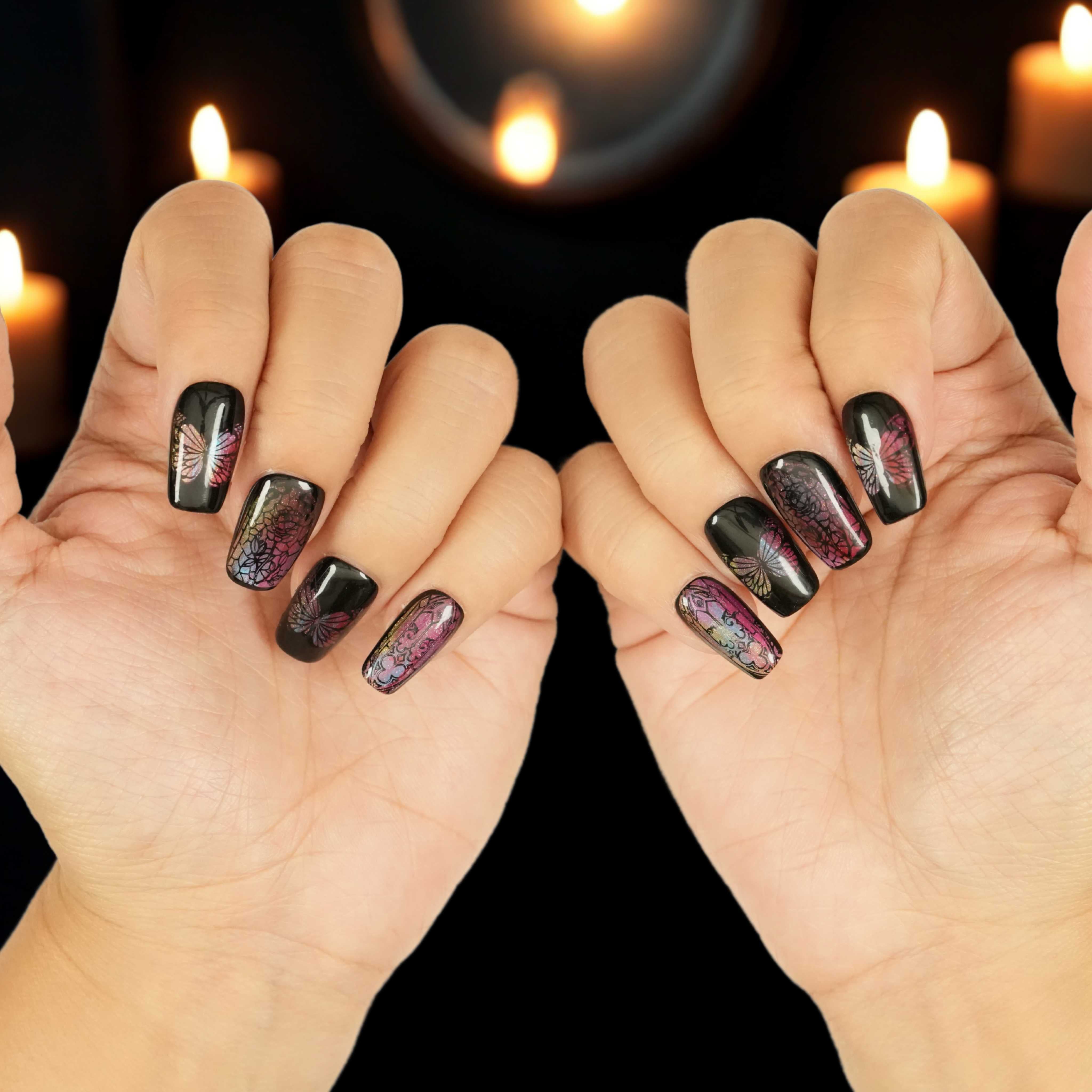 Reusable press on nails Australia with black butterfly designs and pink-purple shimmer, displayed on both hands against candlelit background