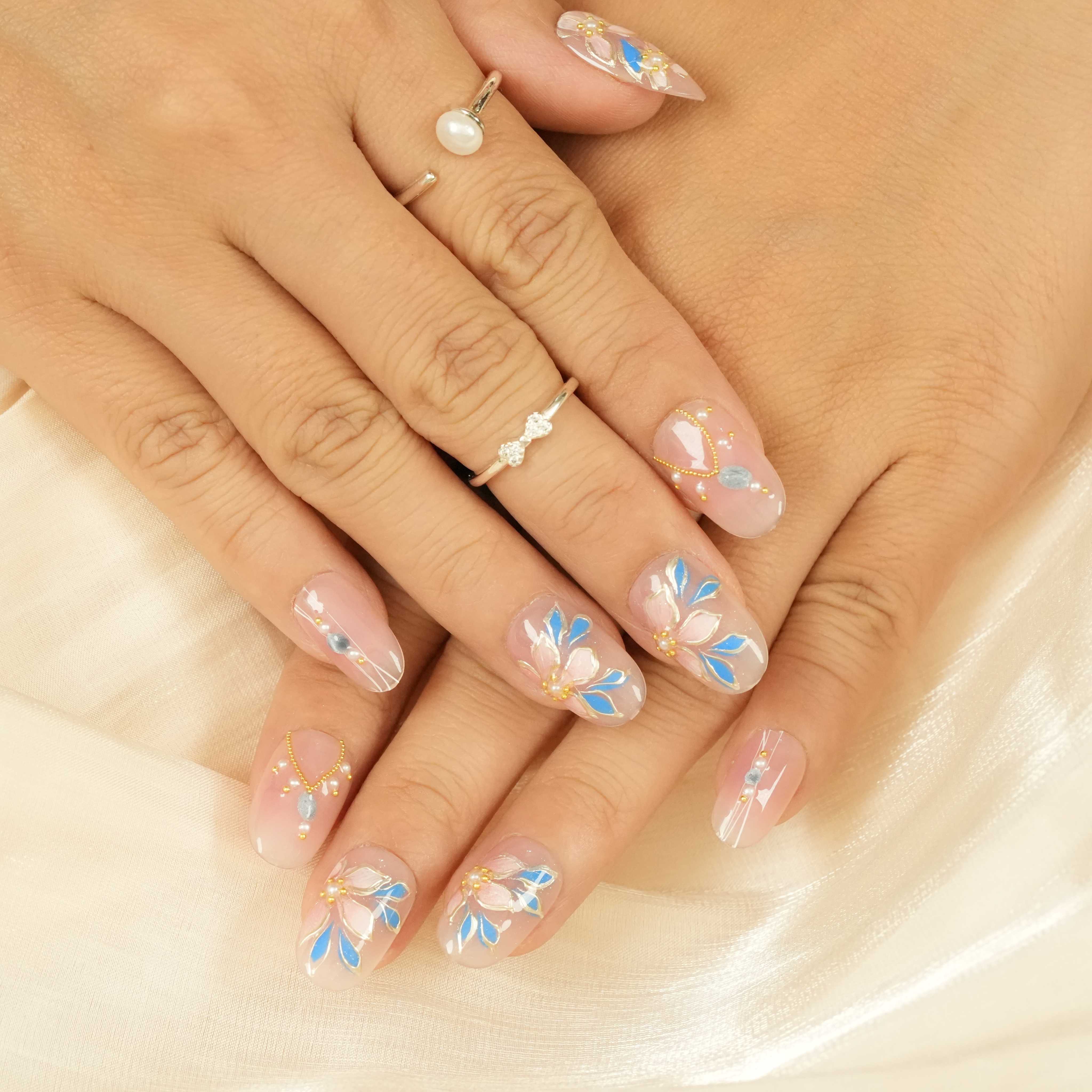 Elegant floral press on nails Adelaide with blue and white petals, accented with gold charms and delicate nude base