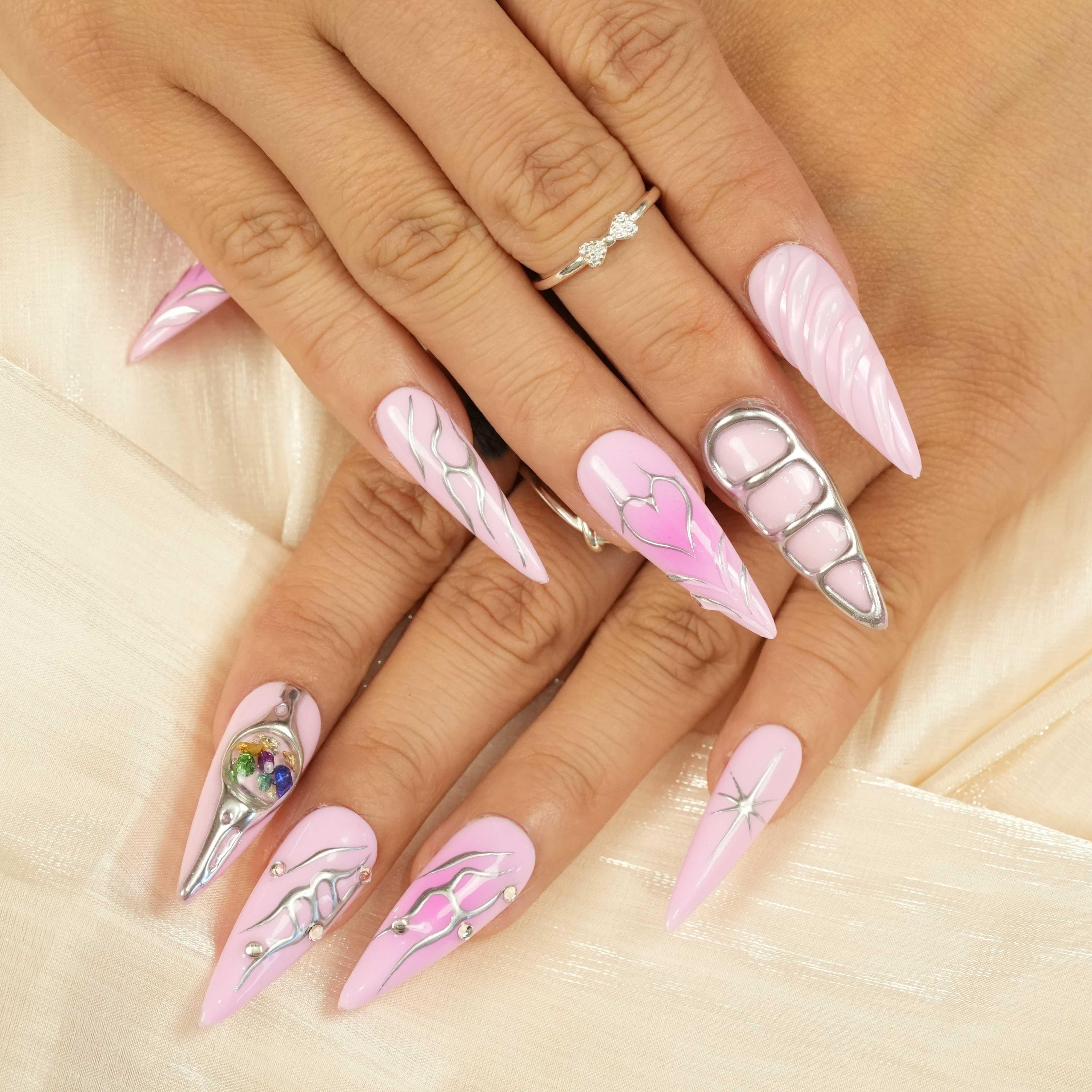 Hand with pink press on nails featuring chrome line art, a sculpted heart design, and a silver 3D grid accent