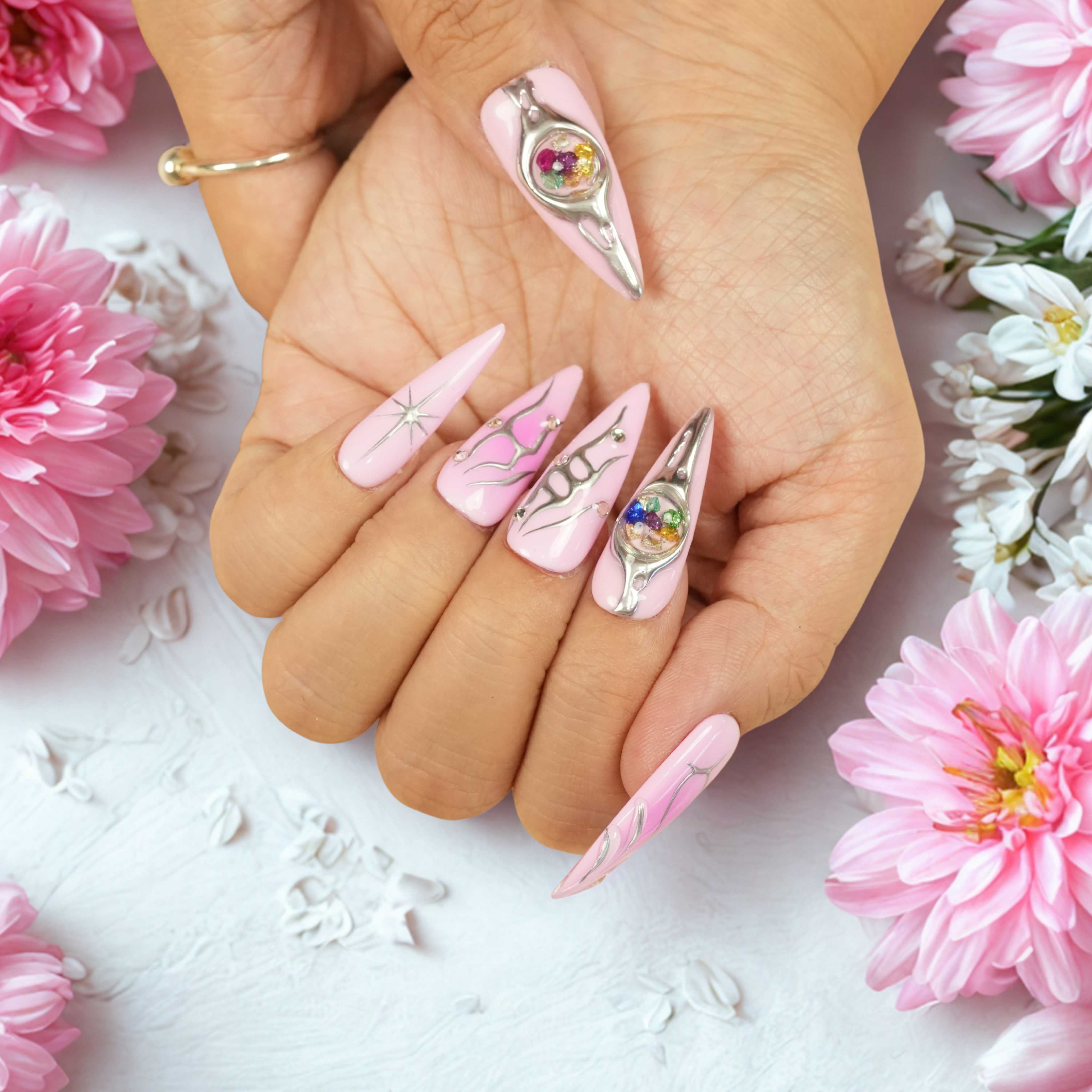 Both hands displaying long stiletto pink press on nails with chrome lines, celestial motifs, and 3D gemstone spheres