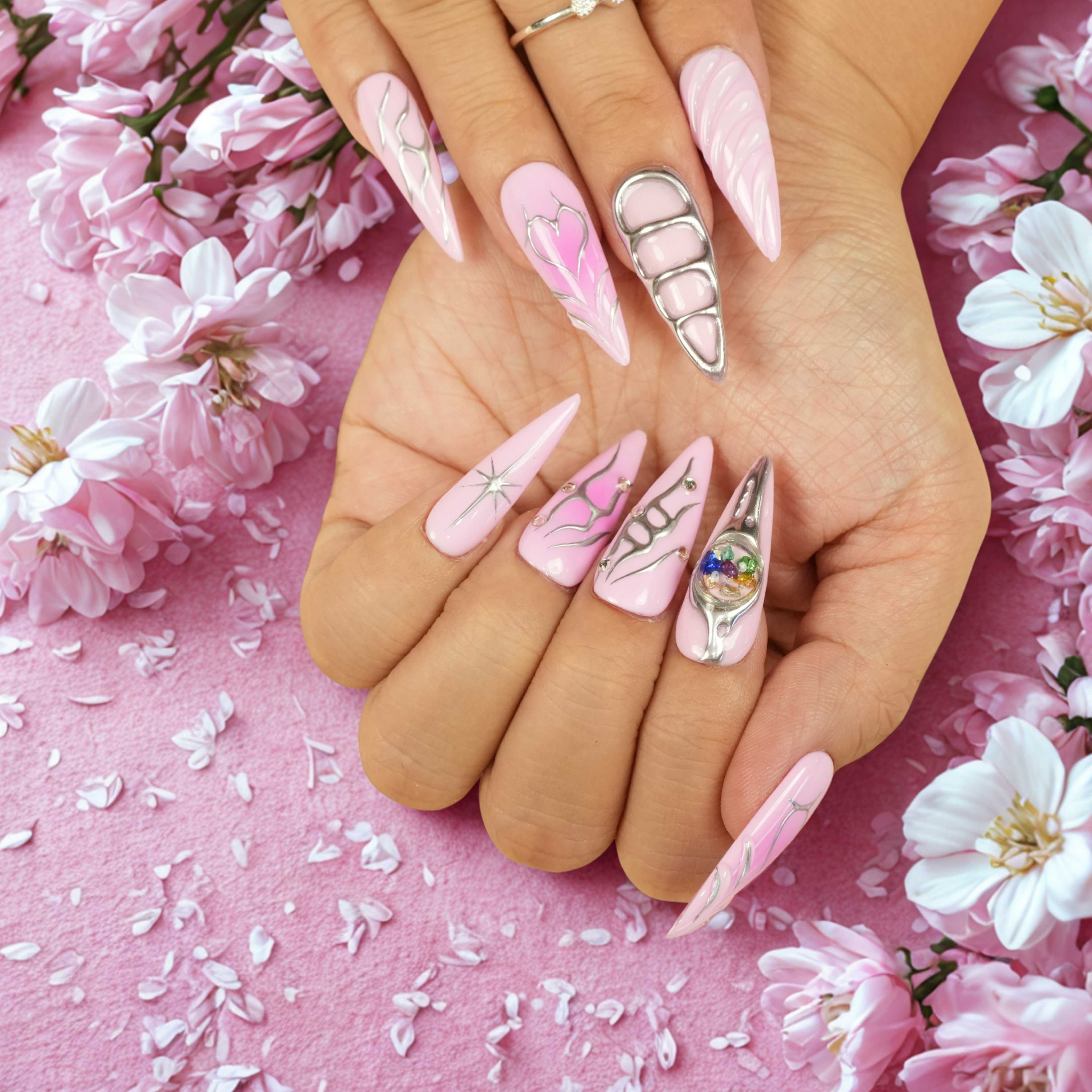 Hand with floral background showing pink press on nails, silver line designs, and a cosmic 3D orb accent