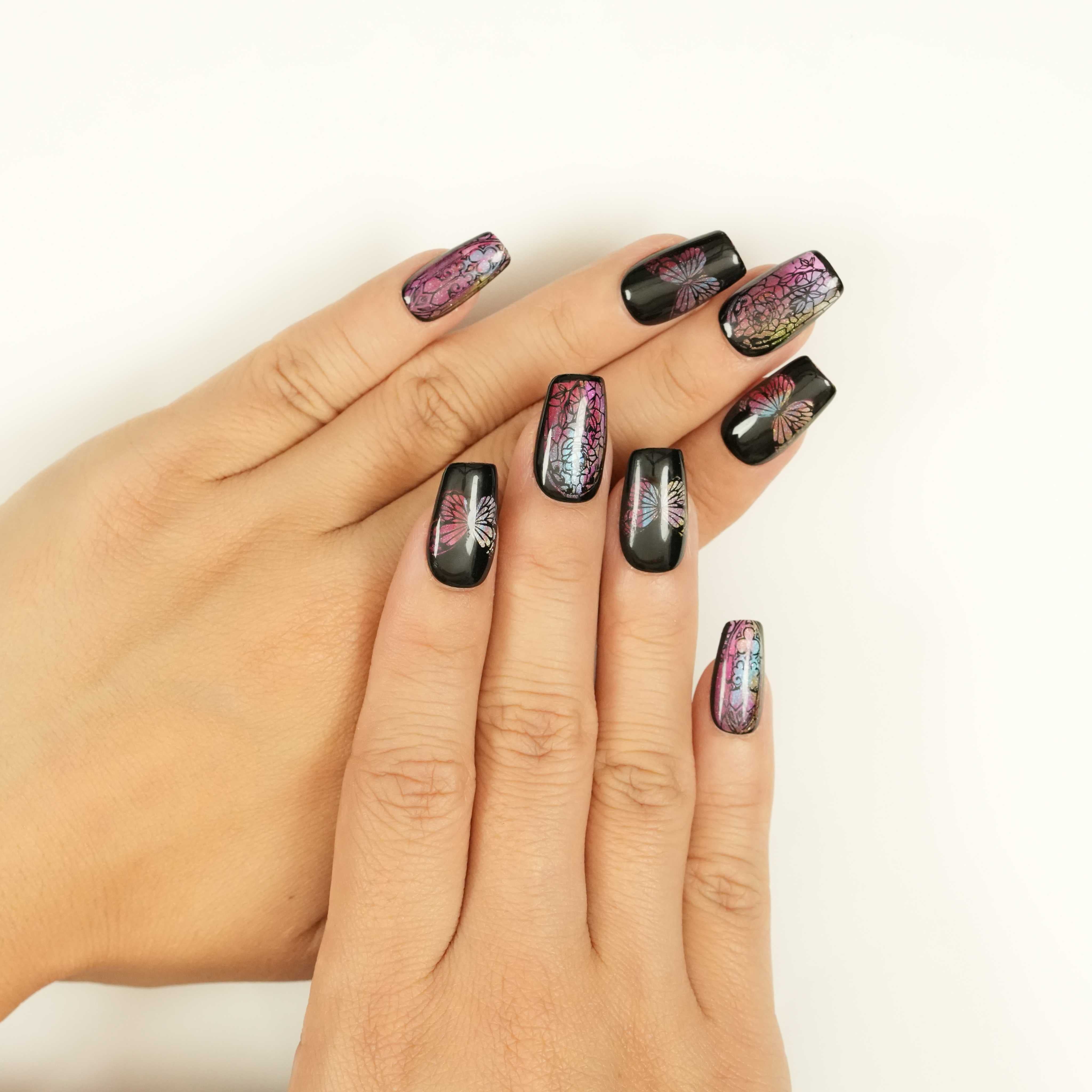 Reusable press on nail shown on thumb featuring butterfly wing design with pink shimmer and black high-gloss finish