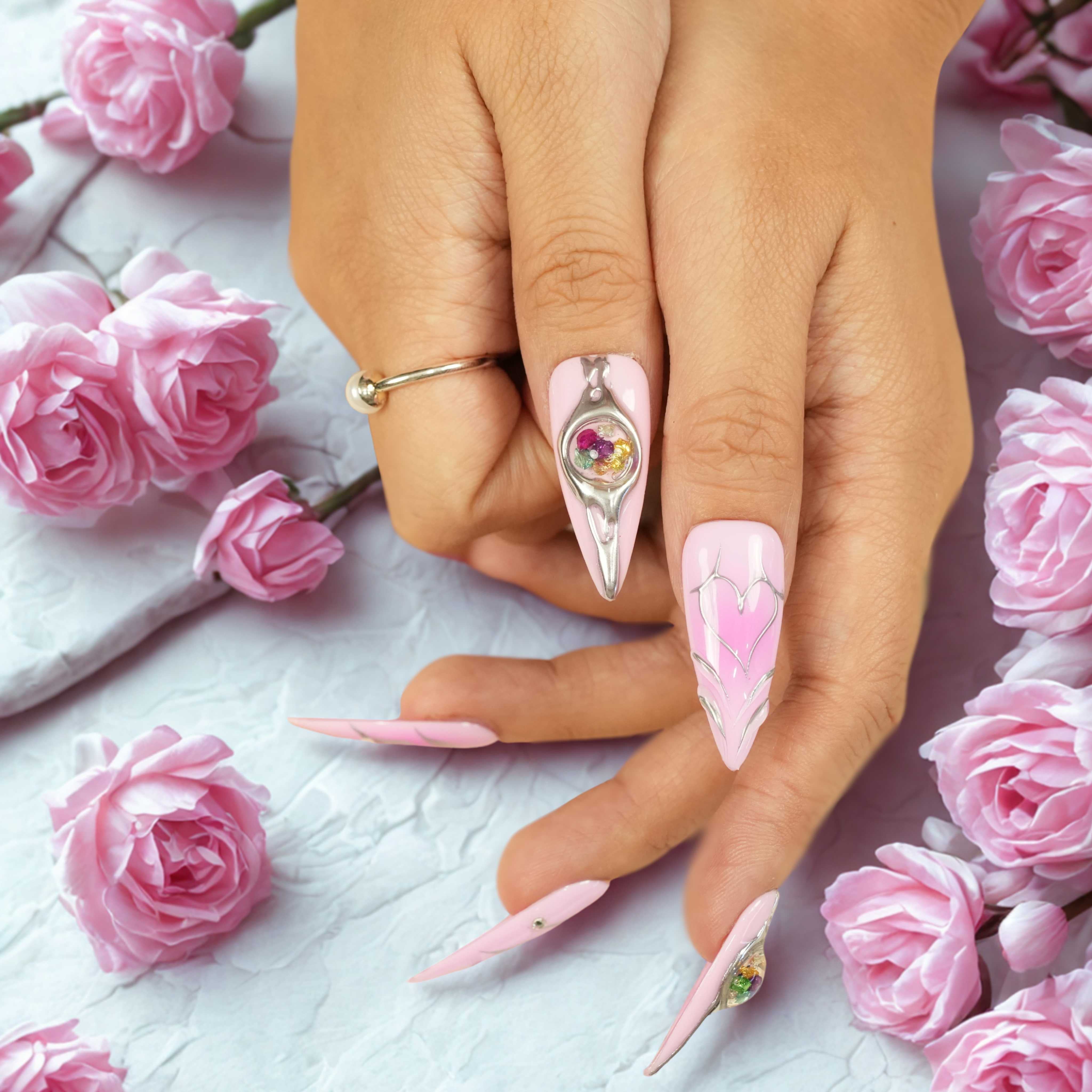 Thumb close-up with pink press on nail, chrome design, and a colorful cosmic orb centerpiece