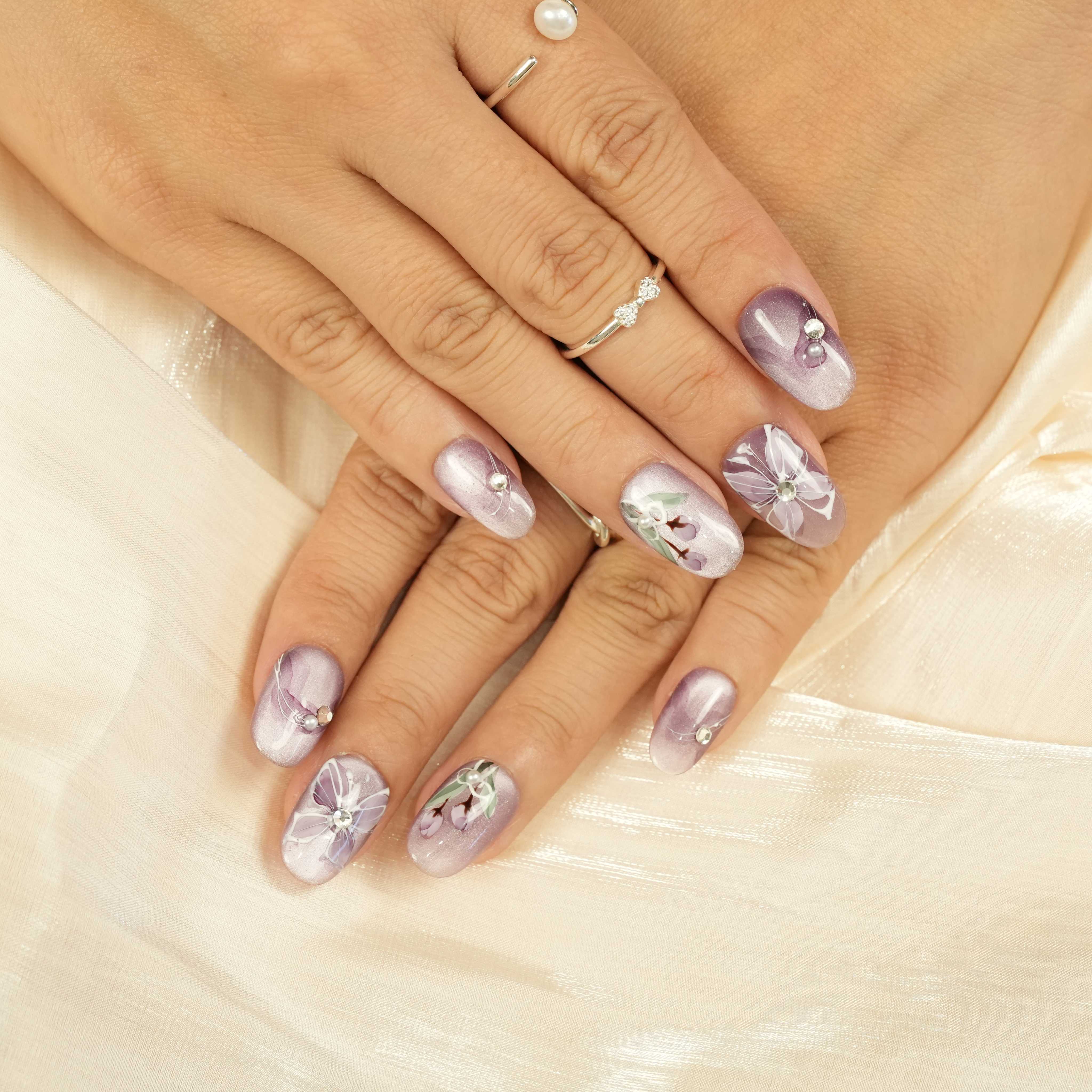 Handcrafted glue-on nails in a soft purple hue featuring elegant floral art and sparkling rhinestone details. Reusable false nails Australia