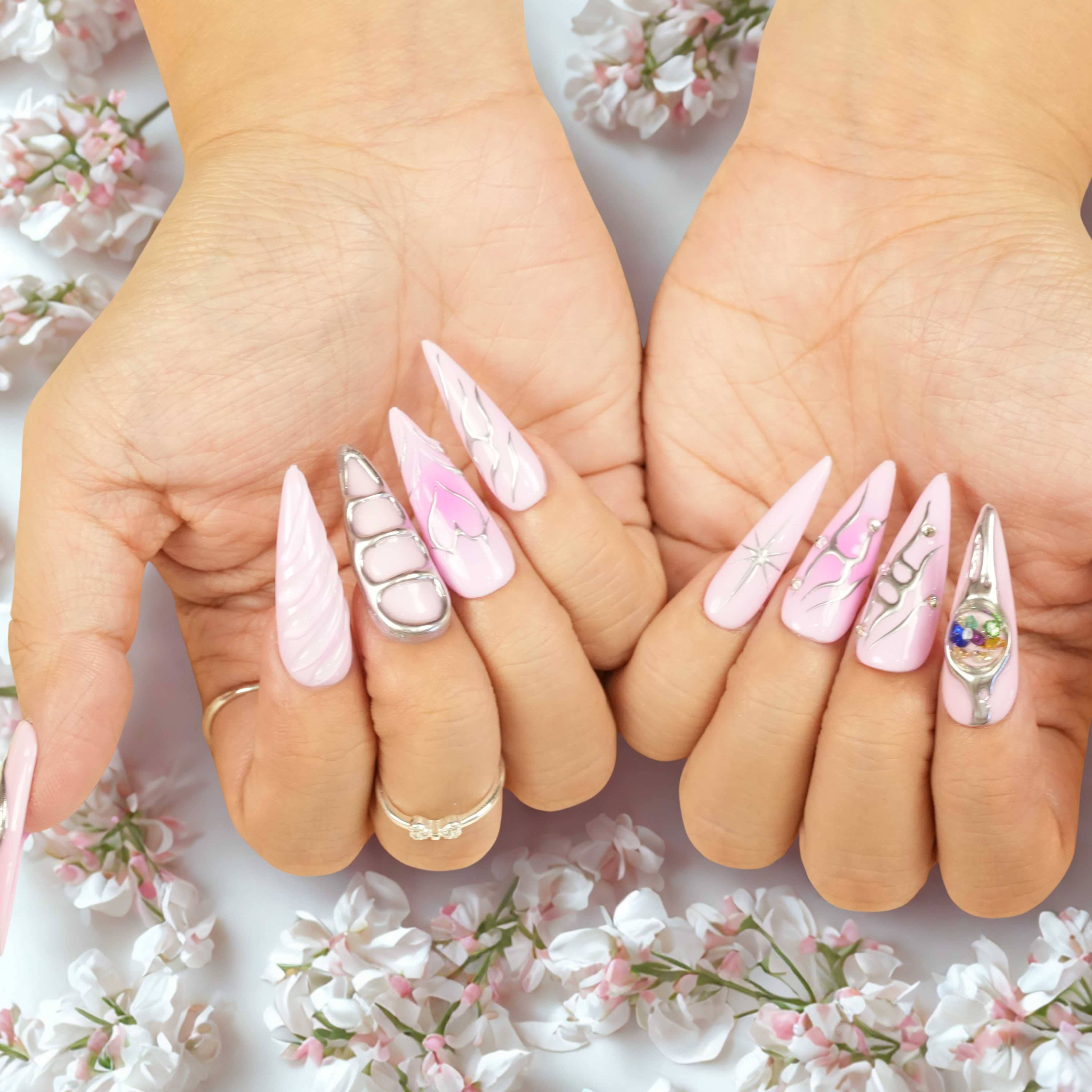 Both hands featuring pink press on nails, silver line accents, 3D orb designs, and long stiletto shapes