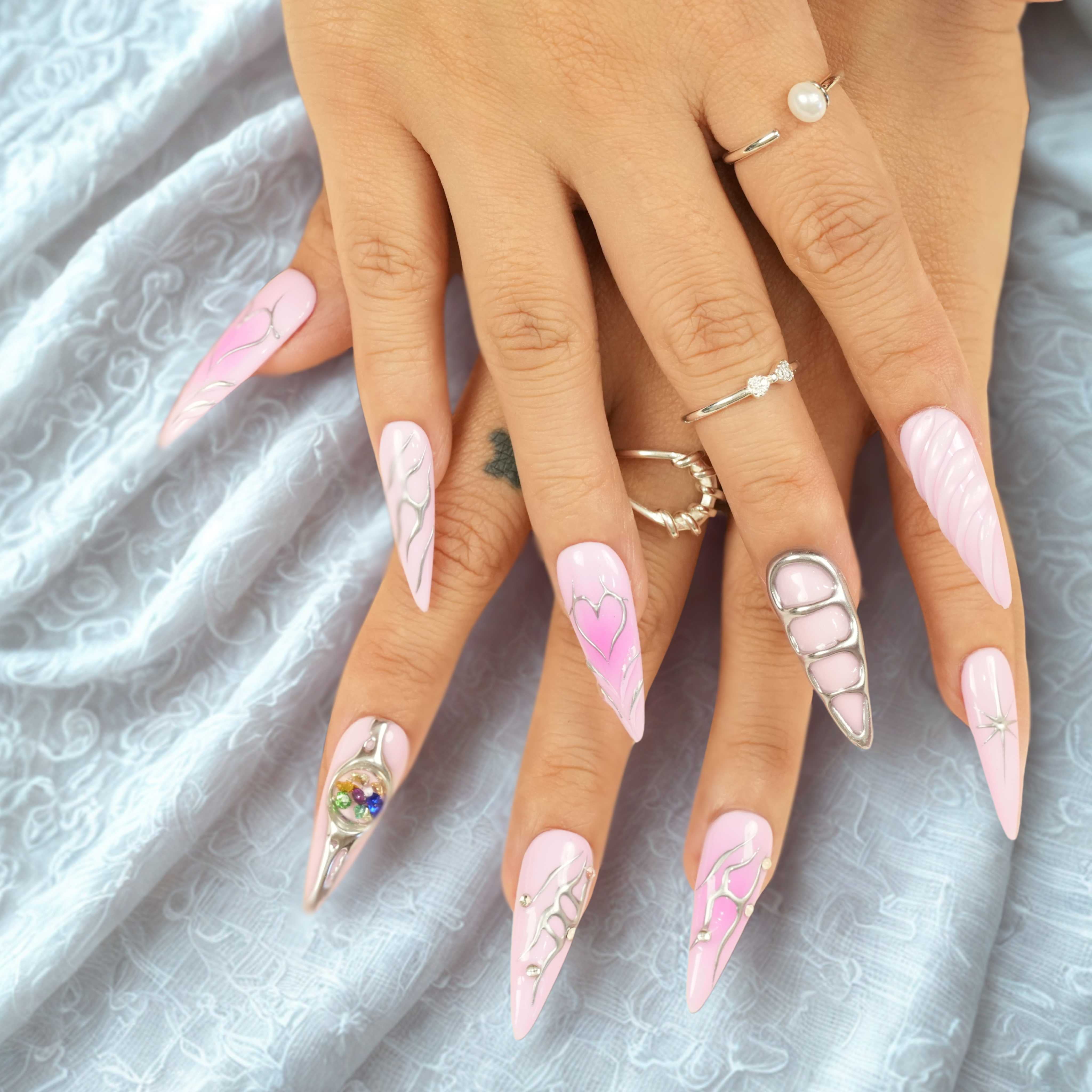 Hand with pink press on nails, including chrome sculpted heart, grid accents, and cosmic gemstone embellishments
