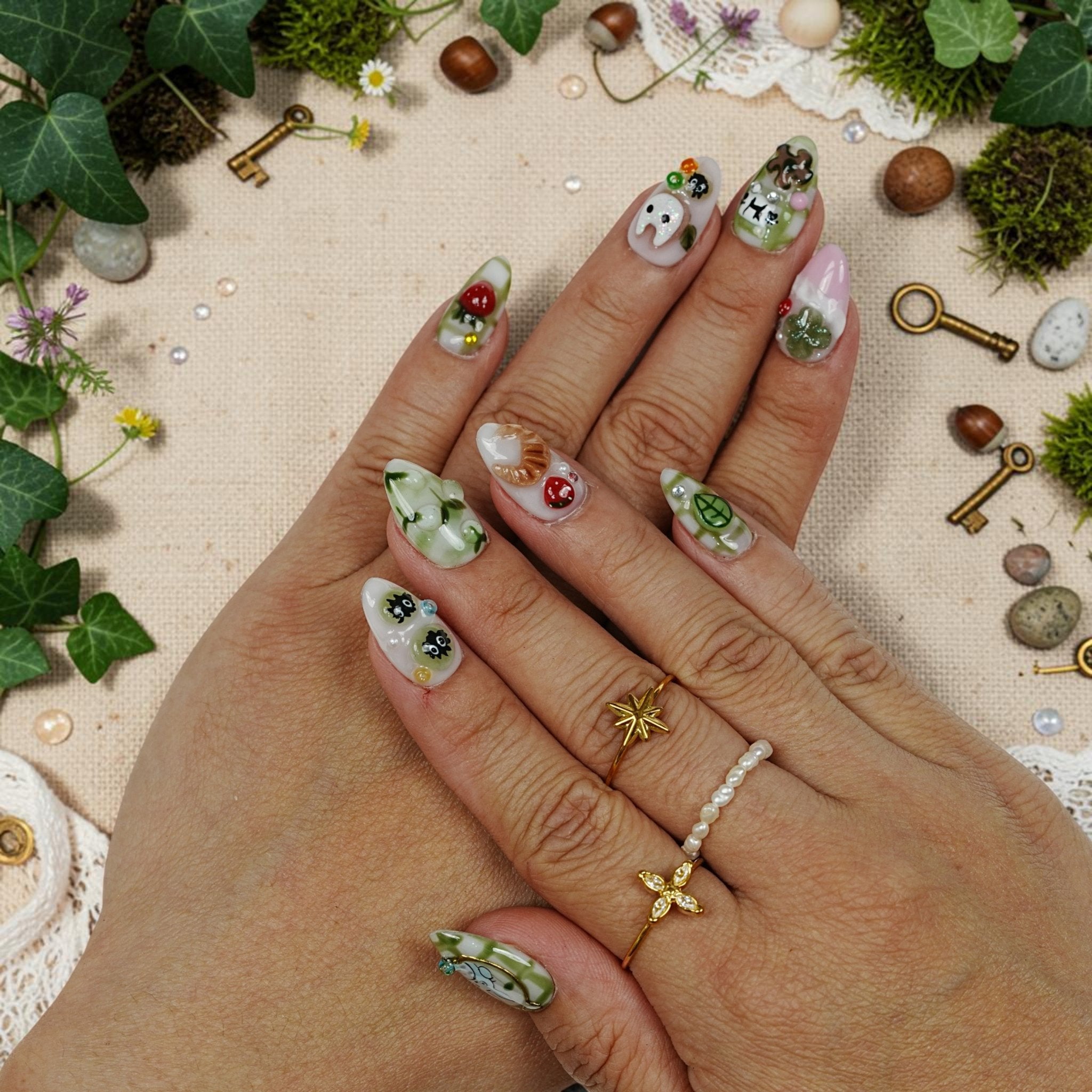 DSC00048 hand wearing matcha press on nails with a fluffy grey forest creature and a 3D strawberry