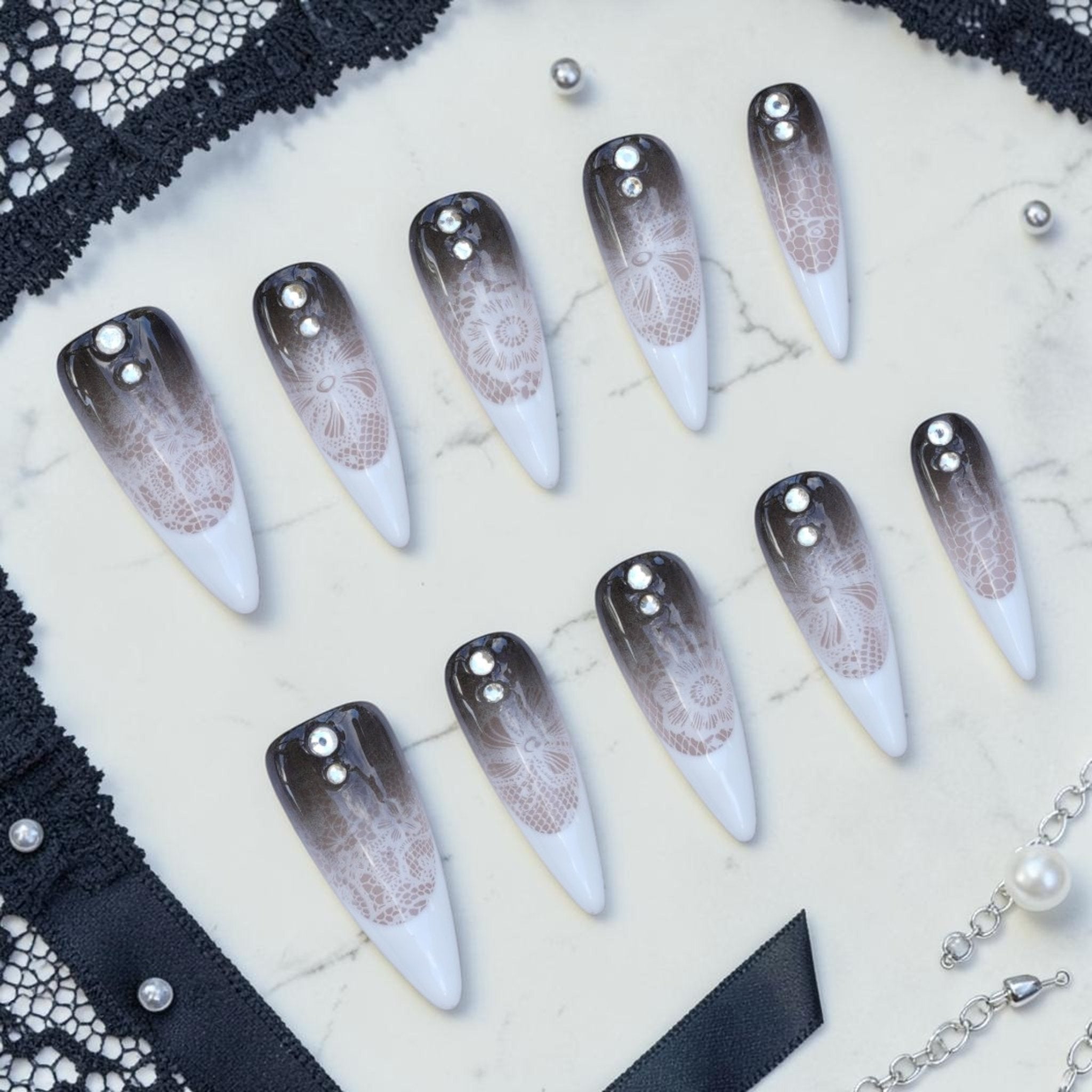 Handmade lace press on nails flat lay in smoky black and white with delicate lace, stiletto tips and crystals