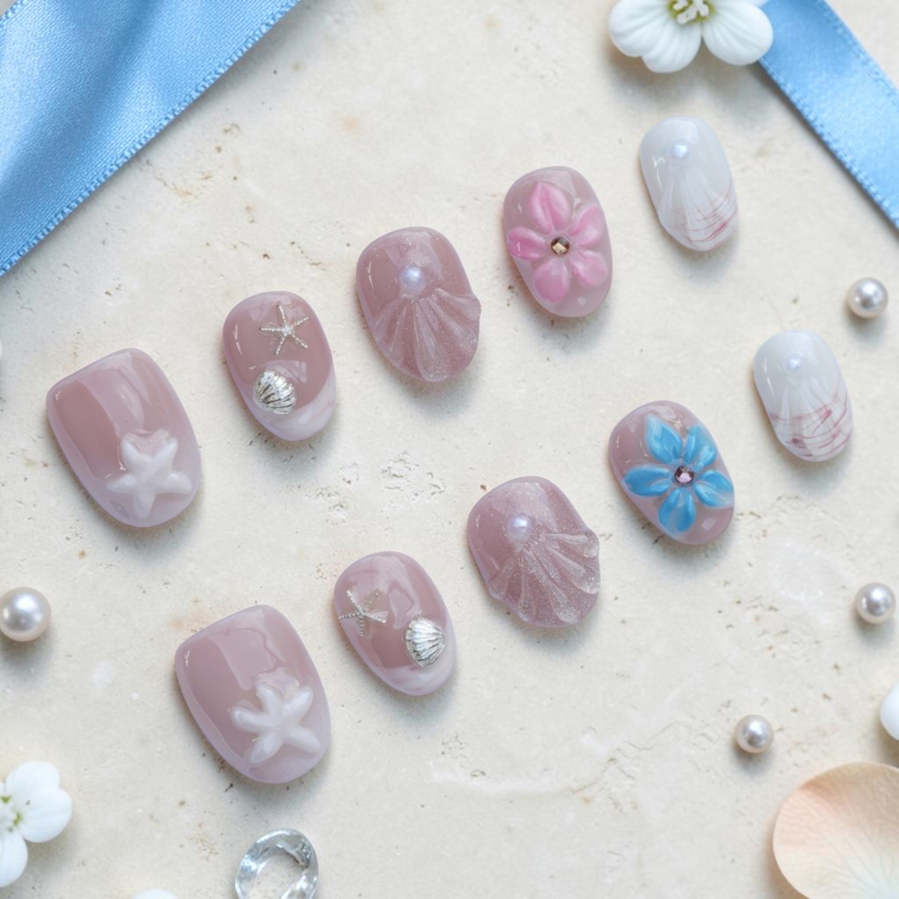 Handmade mermaid press on nails flat lay in soft pink and pearl with 3D shells, starfish and flowers