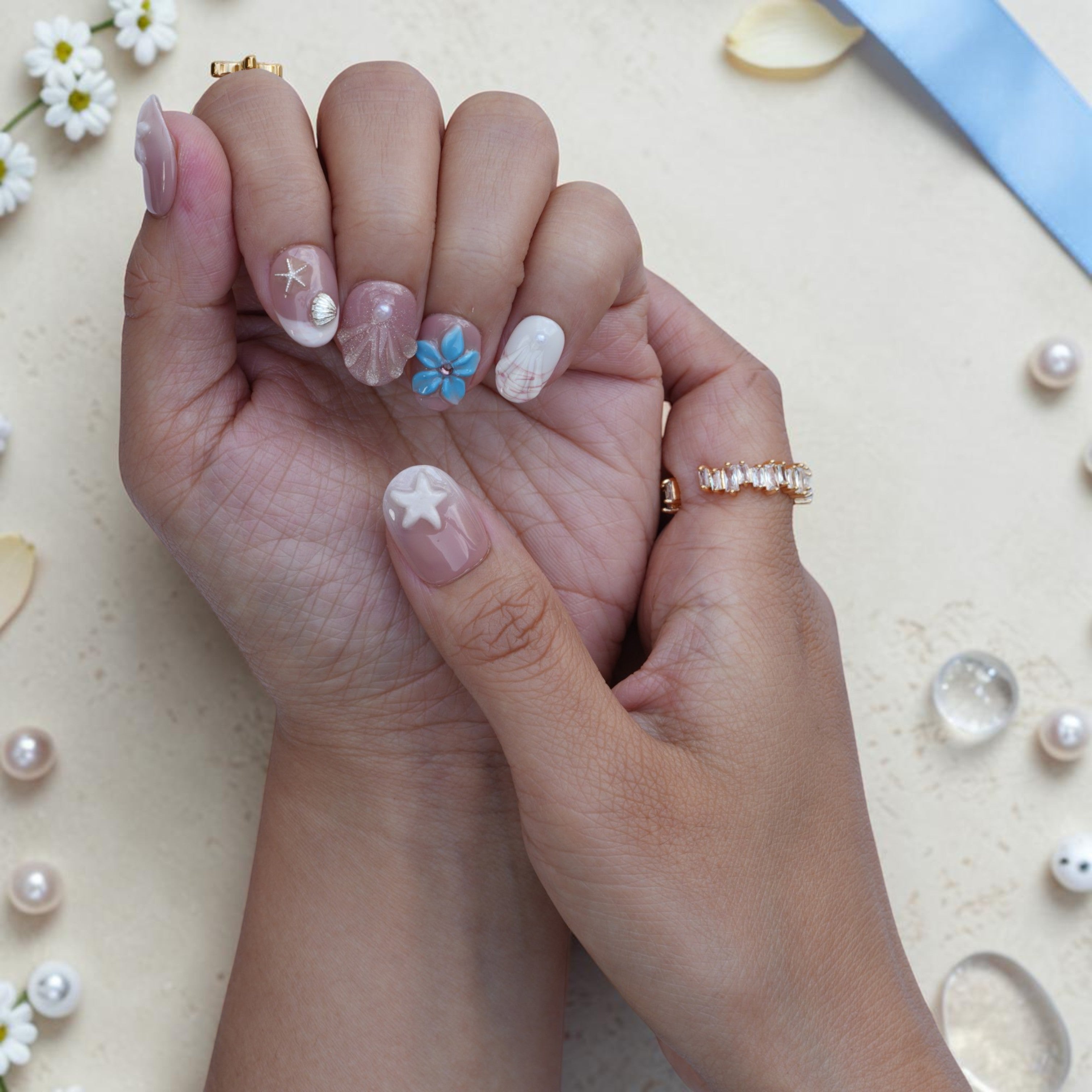 Short round pearl press on nails with 3D shell and starfish styled on hand with gold rings