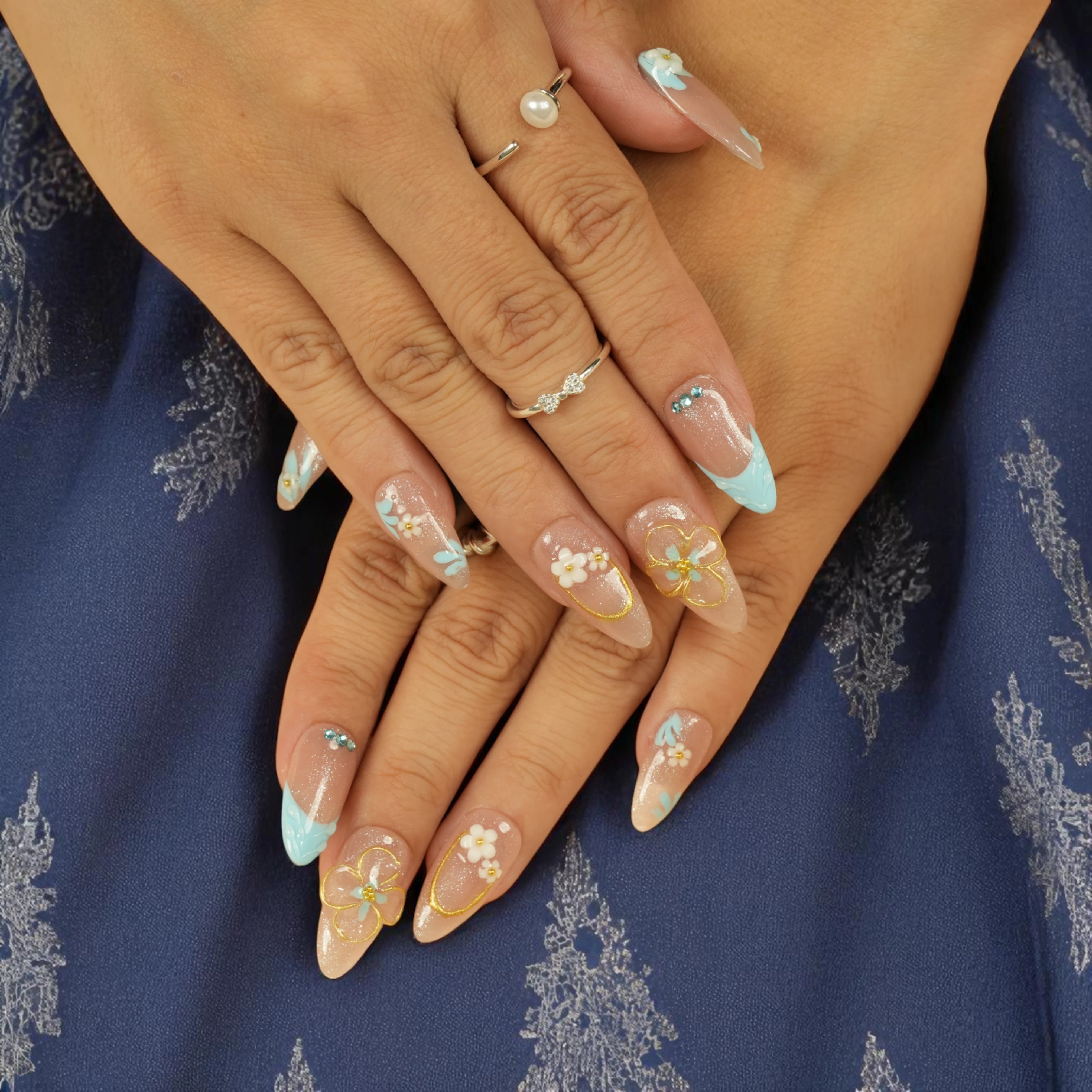Model wearing pastel blue floral false nails with hand-painted blossoms on nude base
