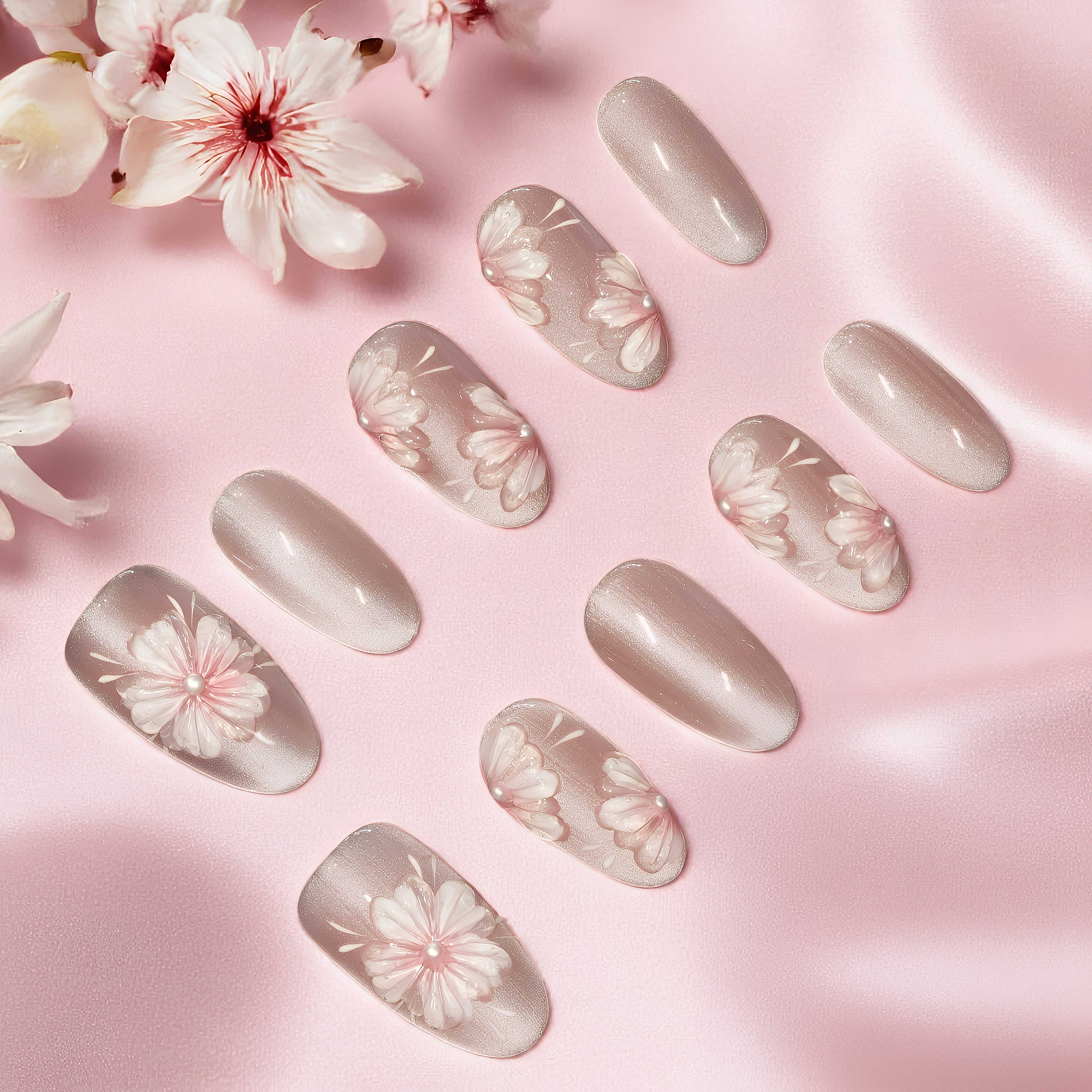 Soft pink floral press on nails with pearl accents, displayed on a satin pink background.