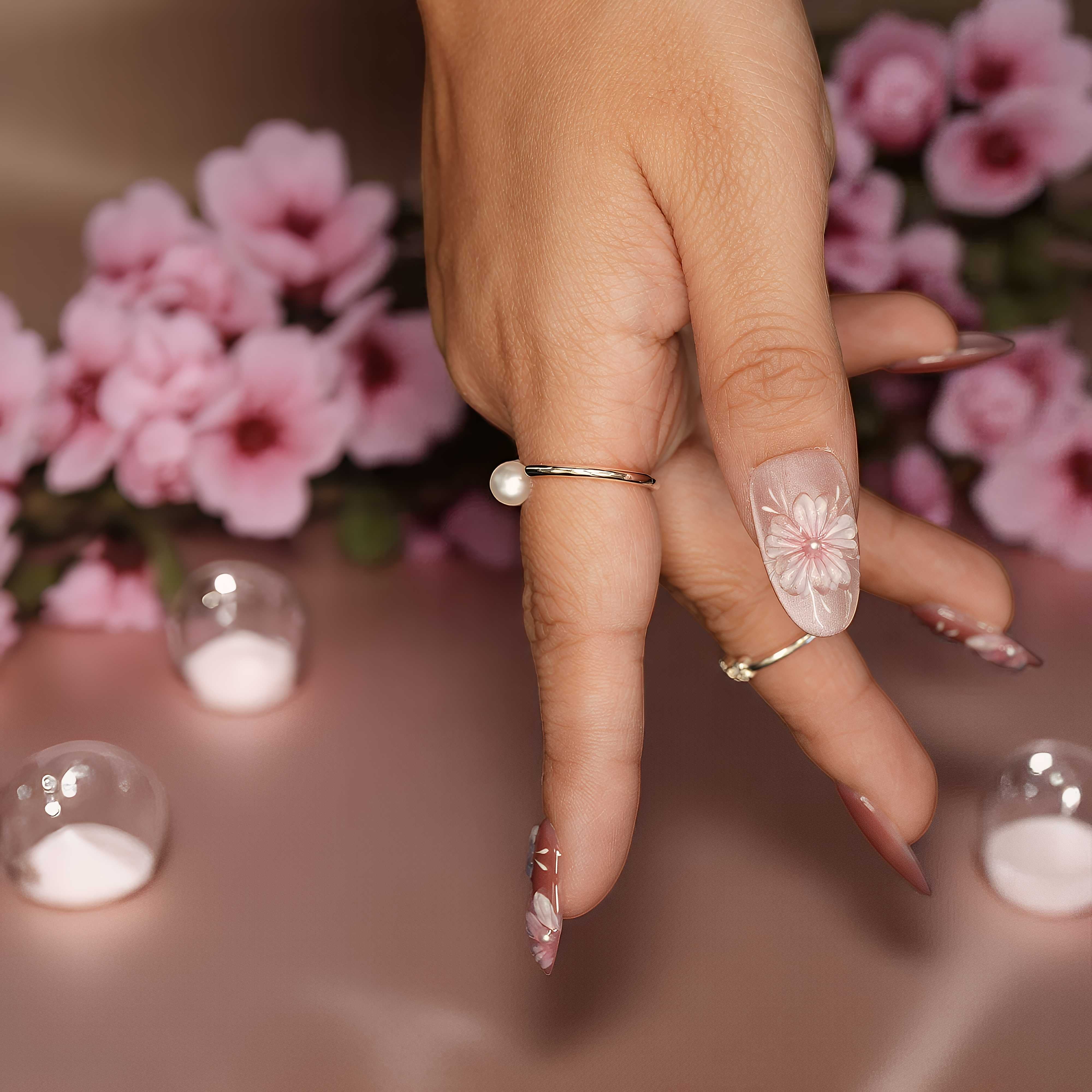 Soft pink false nails with hand-painted floral design, shown on both hands with petal props.
