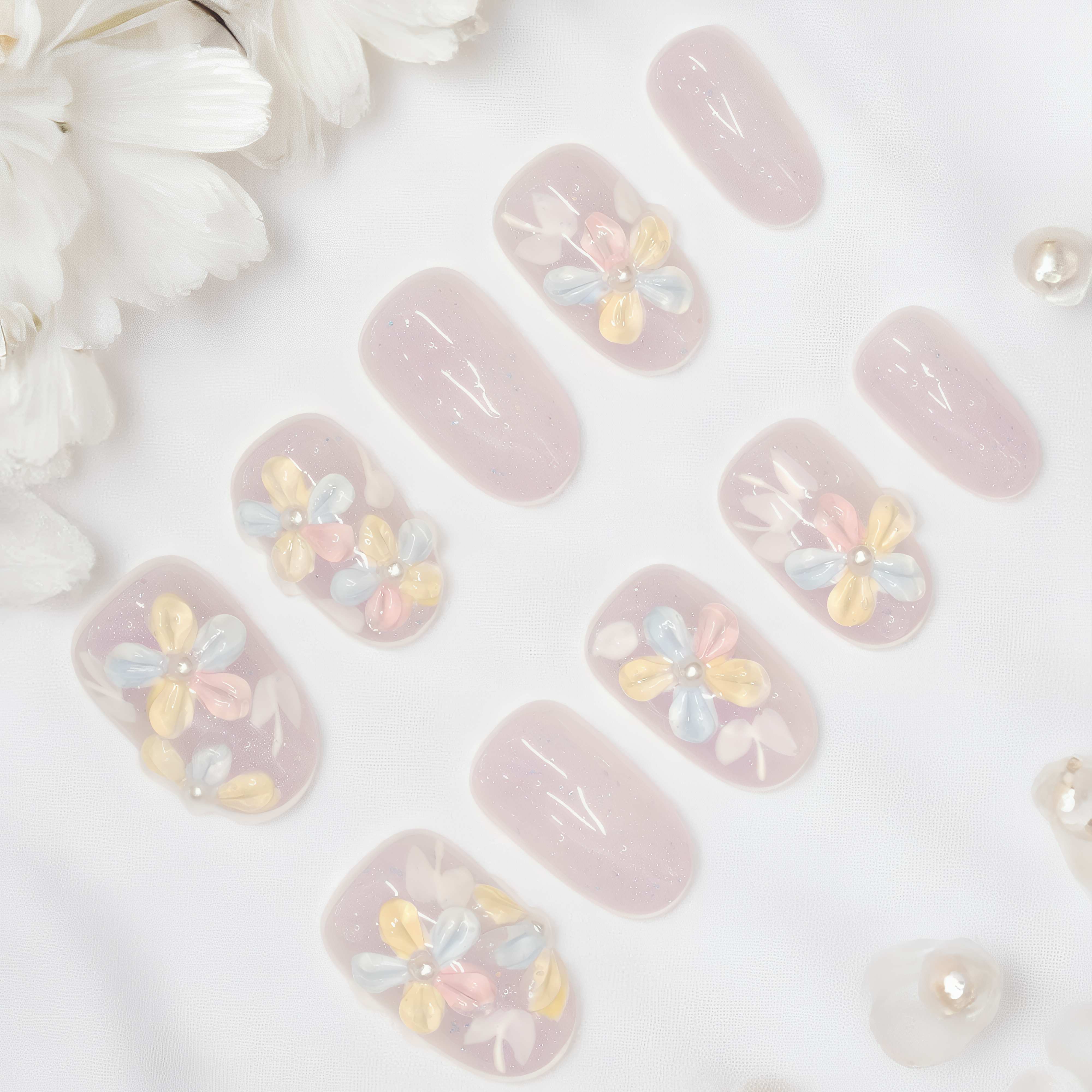 Full set of Bloomlight Daydream press on nails laid out flat on white silk background with soft pastel flowers and shimmer detail.