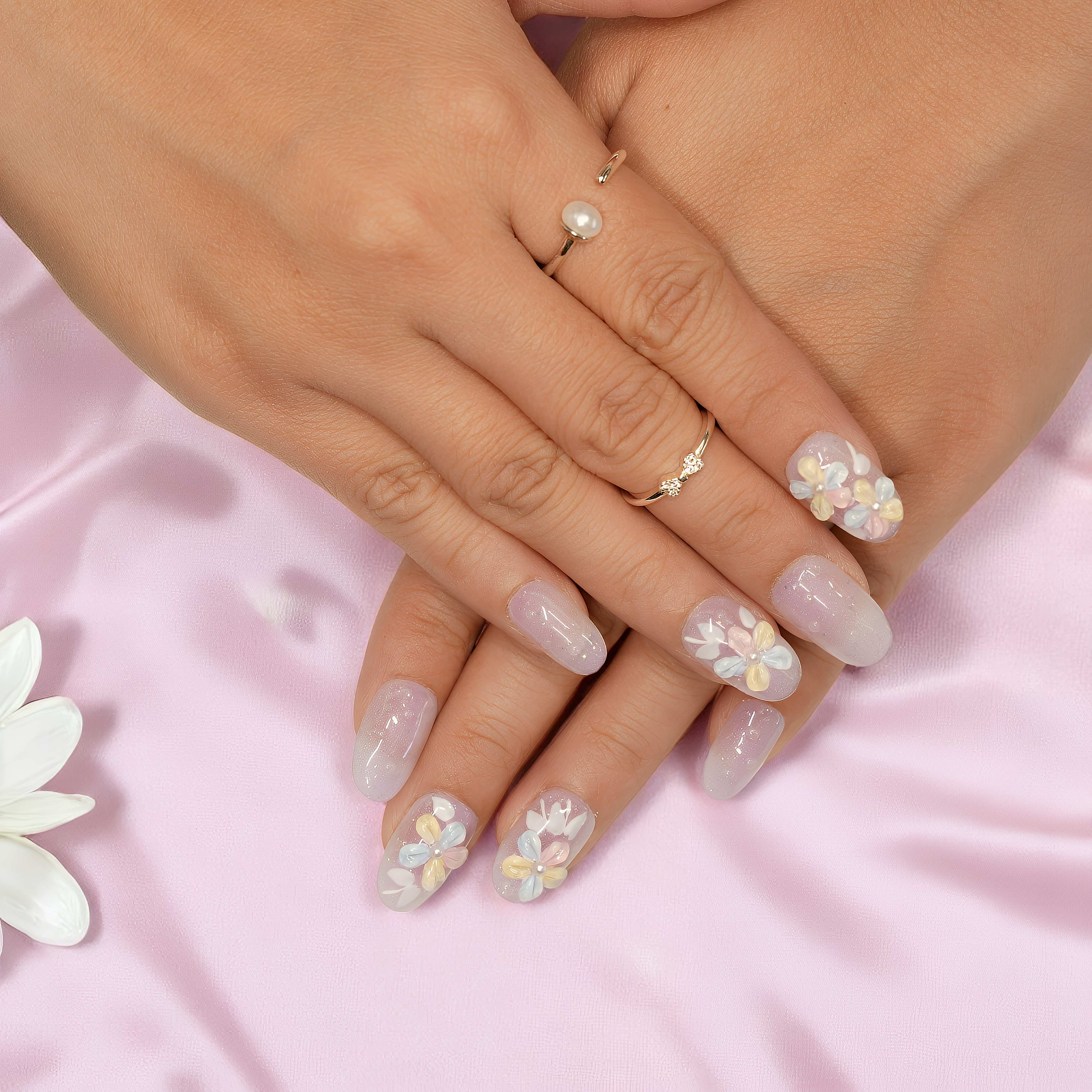 Flat lay of pastel flower press on nails arranged on white fabric with petals, featuring lavender shimmer and 3D daisy details