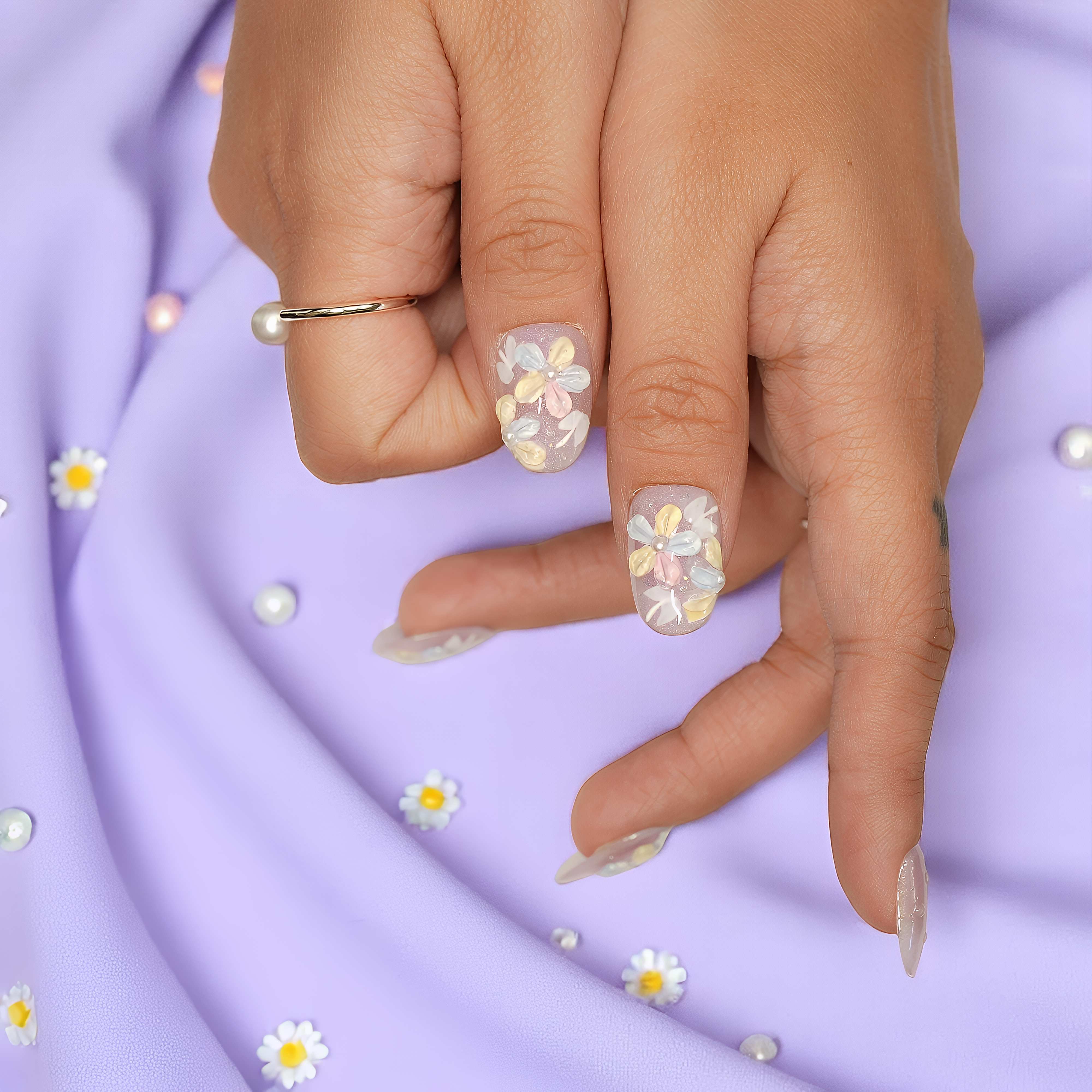 Hands crossed showing Bloomlight Daydream press on nails with soft lavender shimmer and 3D pastel flowers on satin pink background