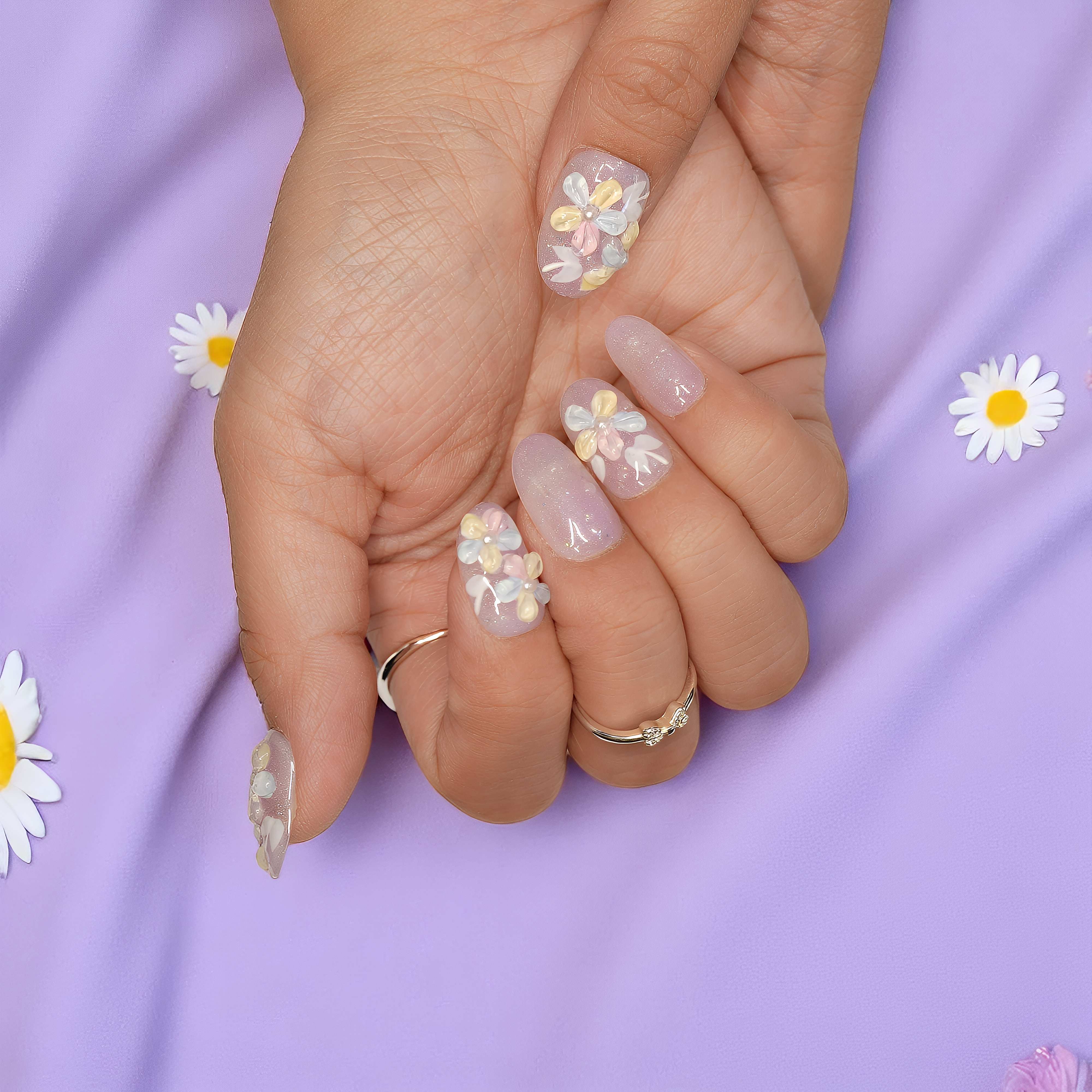 Soft pink background with hands holding daisy-themed press on nails featuring 3D floral accents