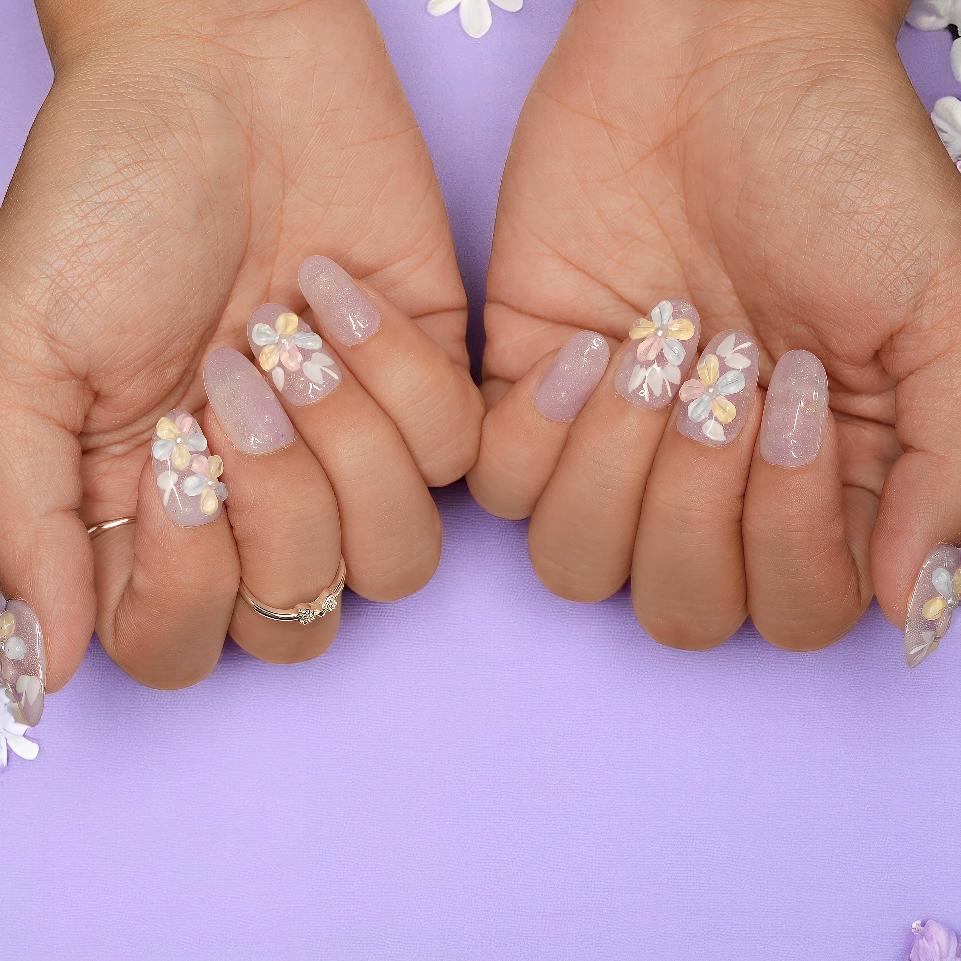 Left hand displaying pastel floral press on nails with shimmer finish, placed gently over lilac daisy fabric