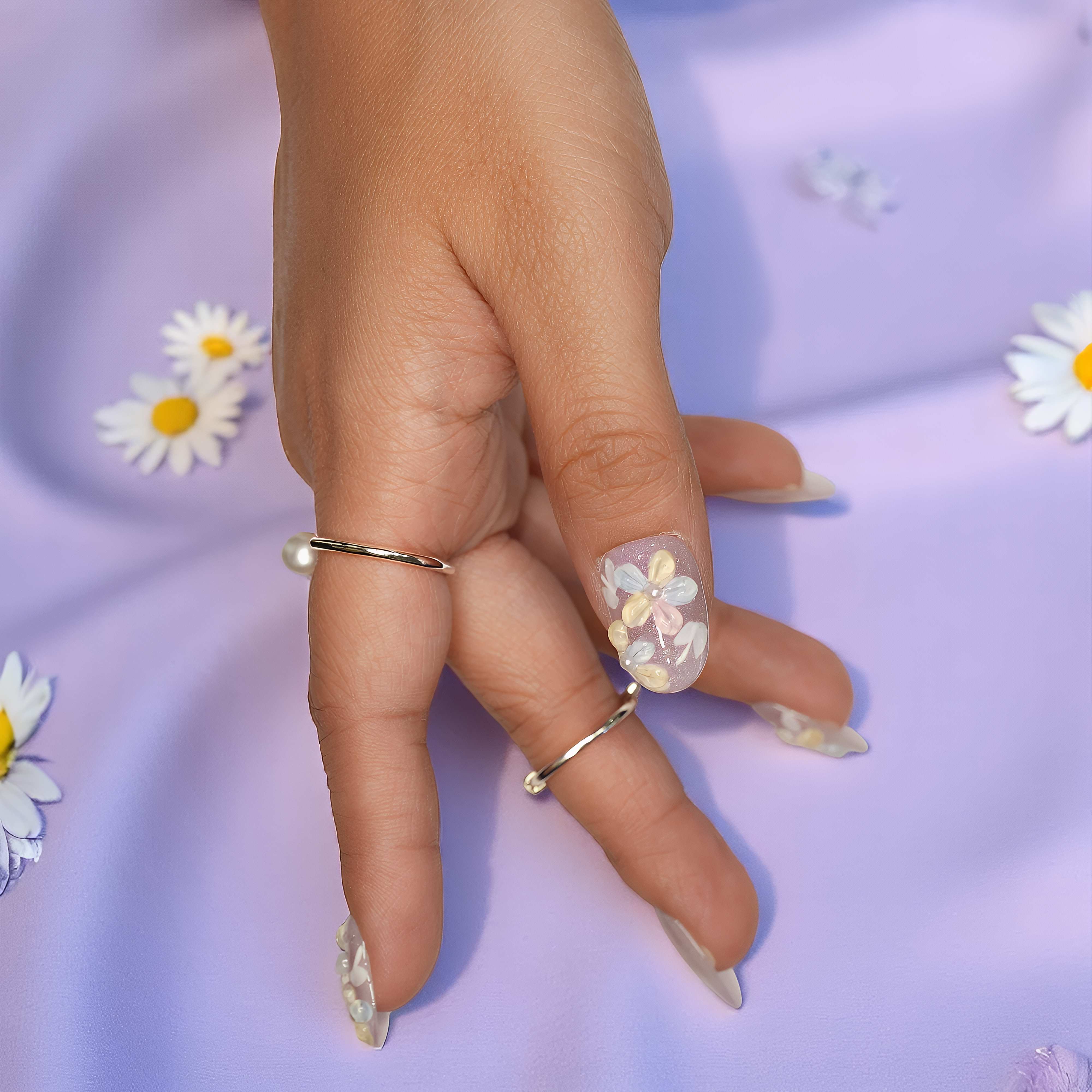 Close-up of thumb nail featuring pastel floral accents with pearl centers on a clear lilac base