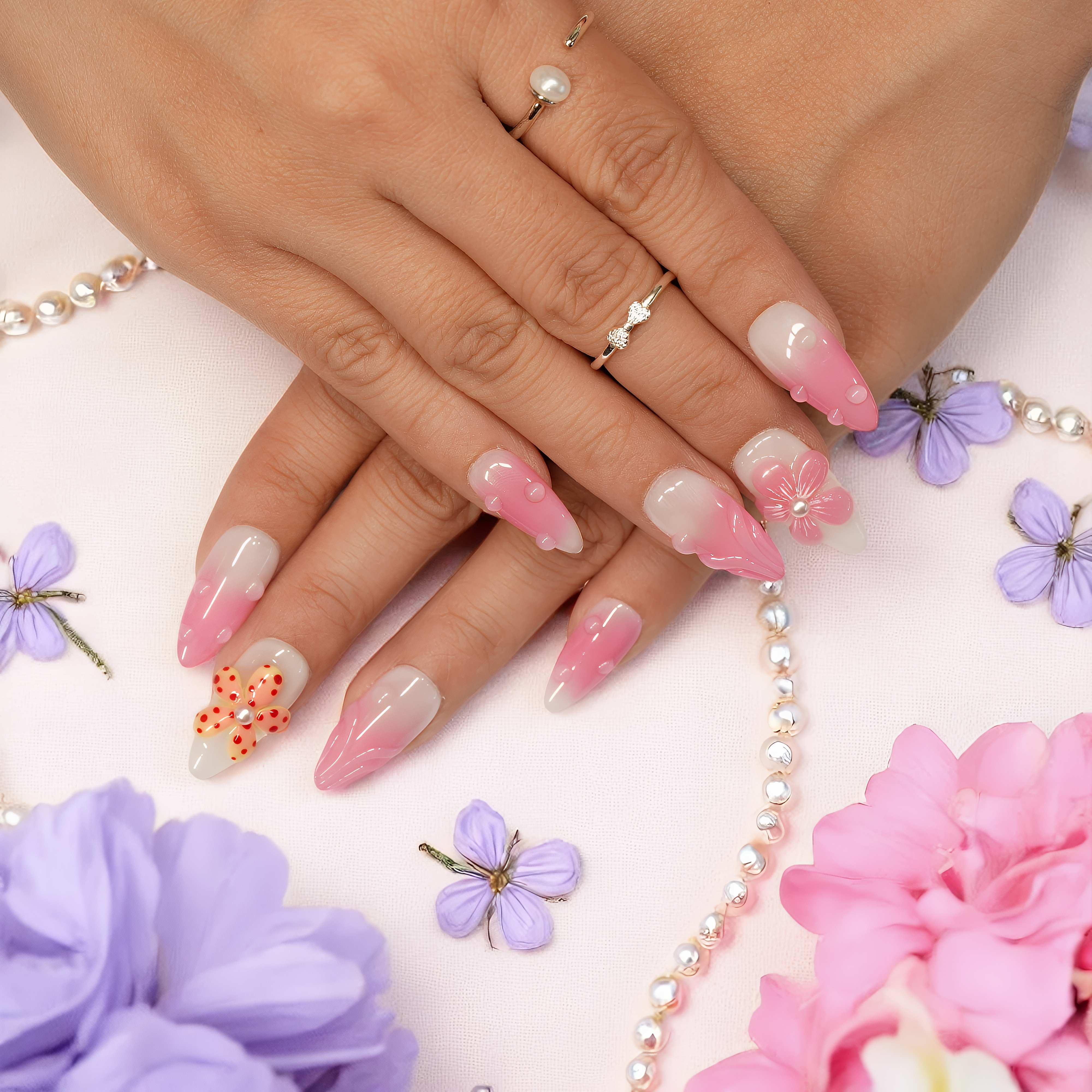 lose-up of hands wearing Petal Pop floral press on nails, showcasing glossy pink ombré tips with raindrop accents