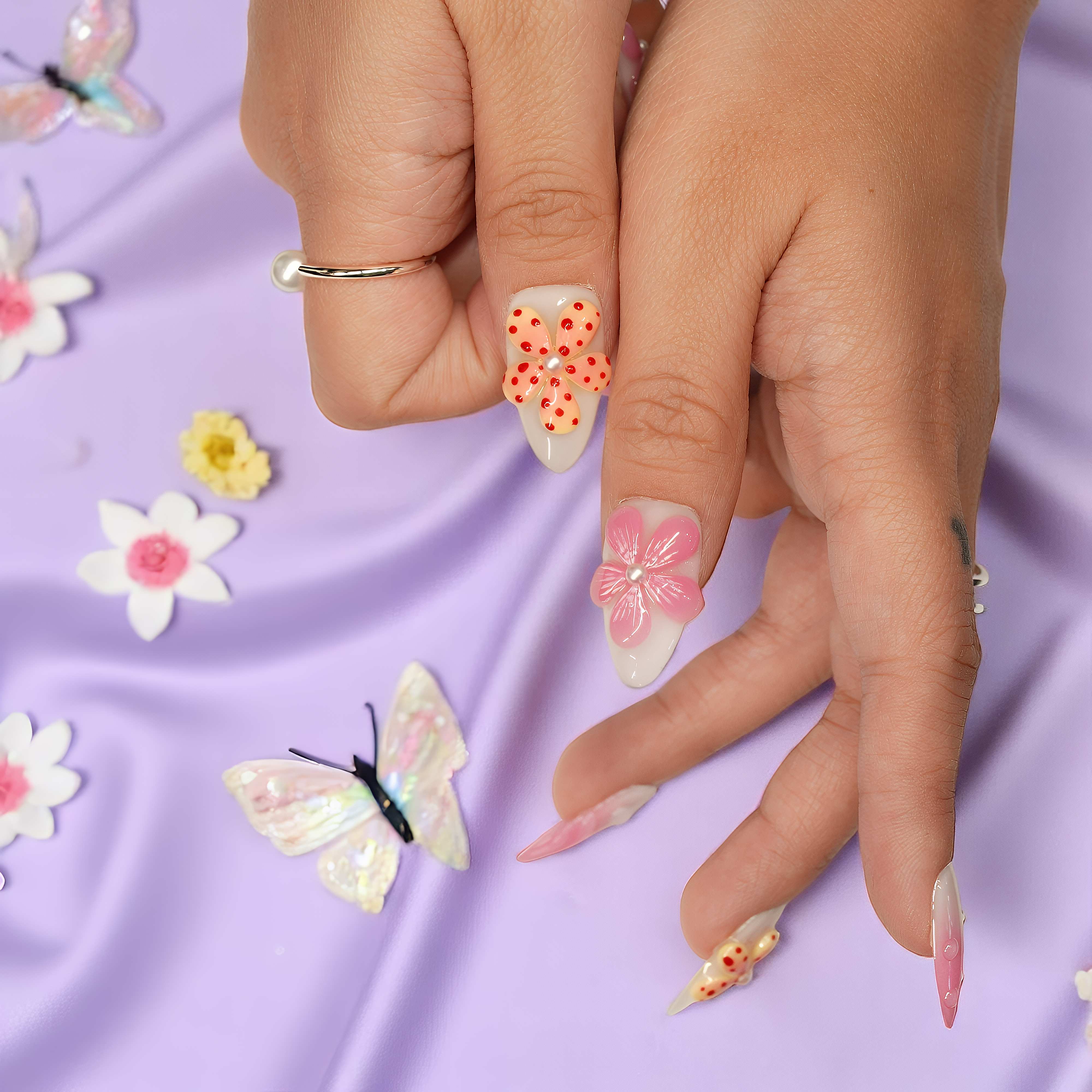 Floral press on nails with orange dotted petals and baby pink flowers, displayed against a lavender fabric