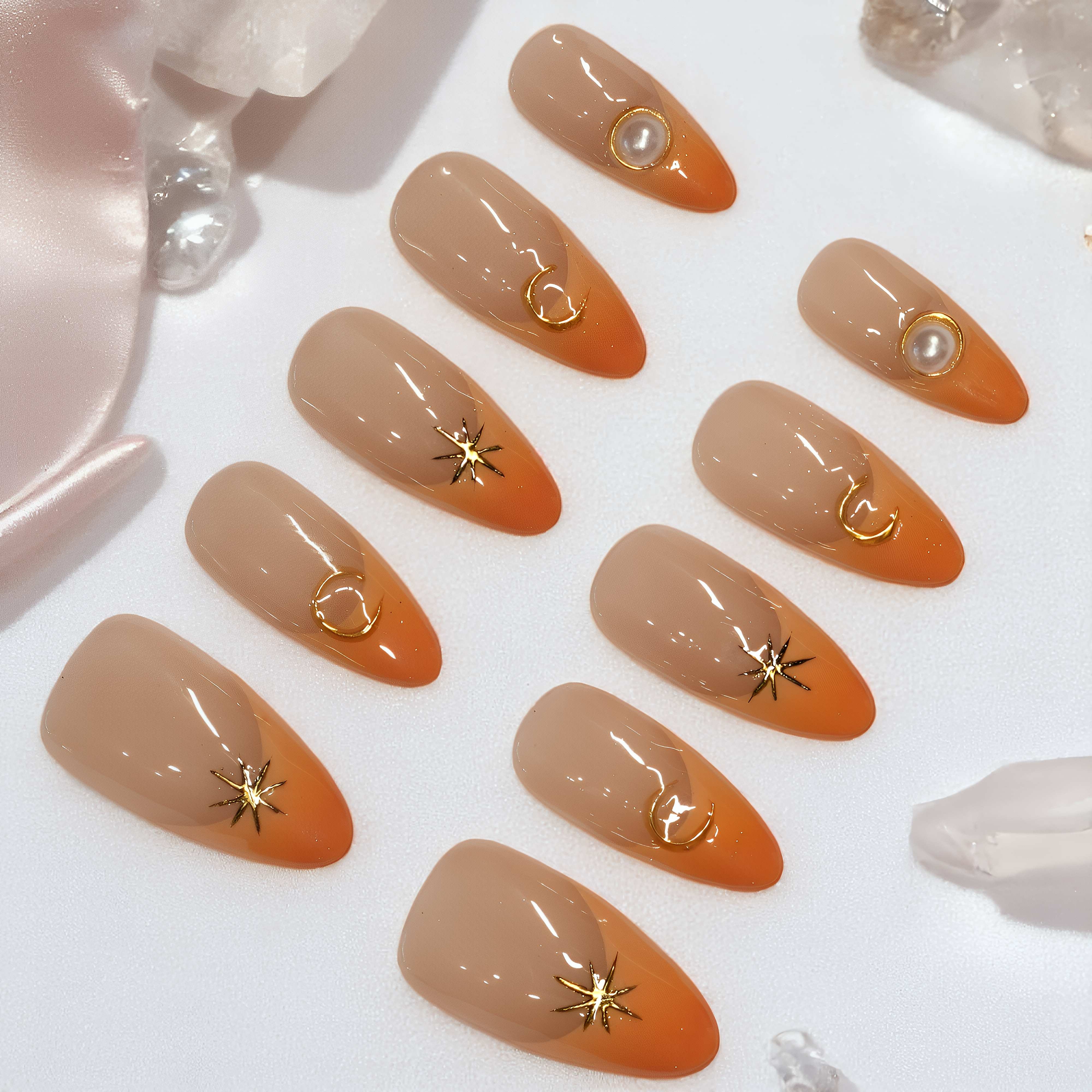 Sunset Nova press on nails laid out, featuring orange French tips with gold star, moon, and pearl embellishments