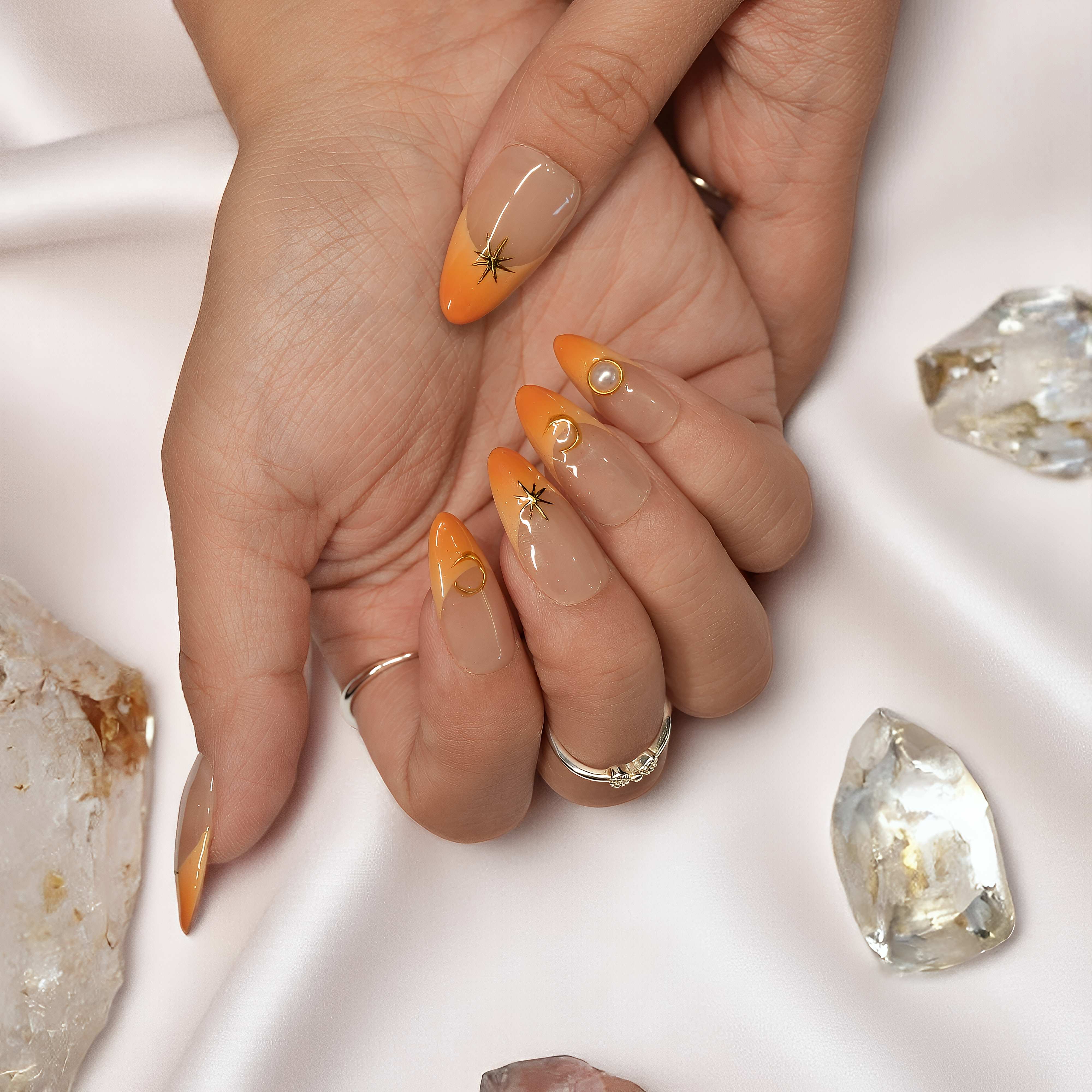 Hand held close-up highlighting orange French tips and a delicate gold star charm