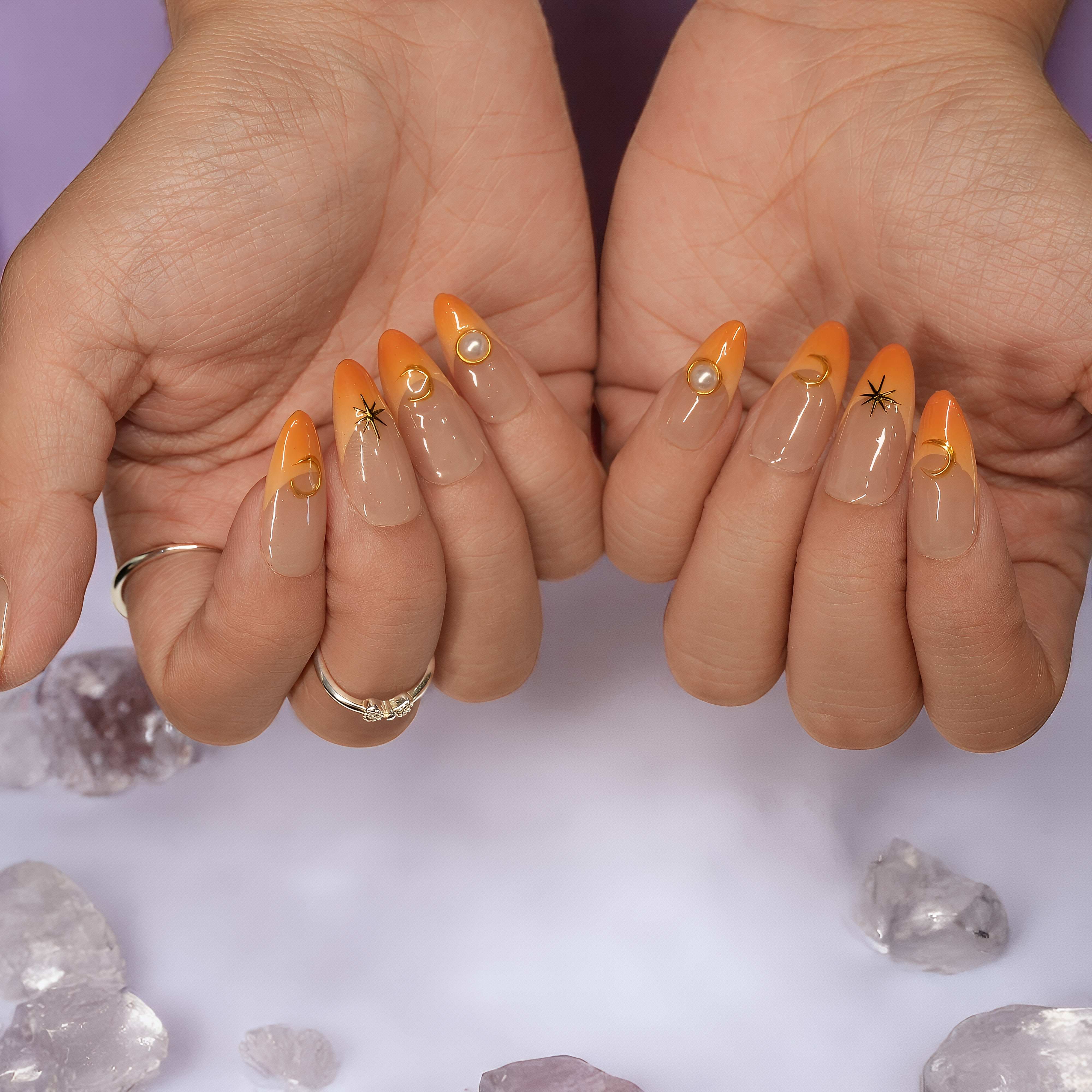 Hands slightly cupped, showing complete Sunset Nova nail set with celestial gold accents and pearls
