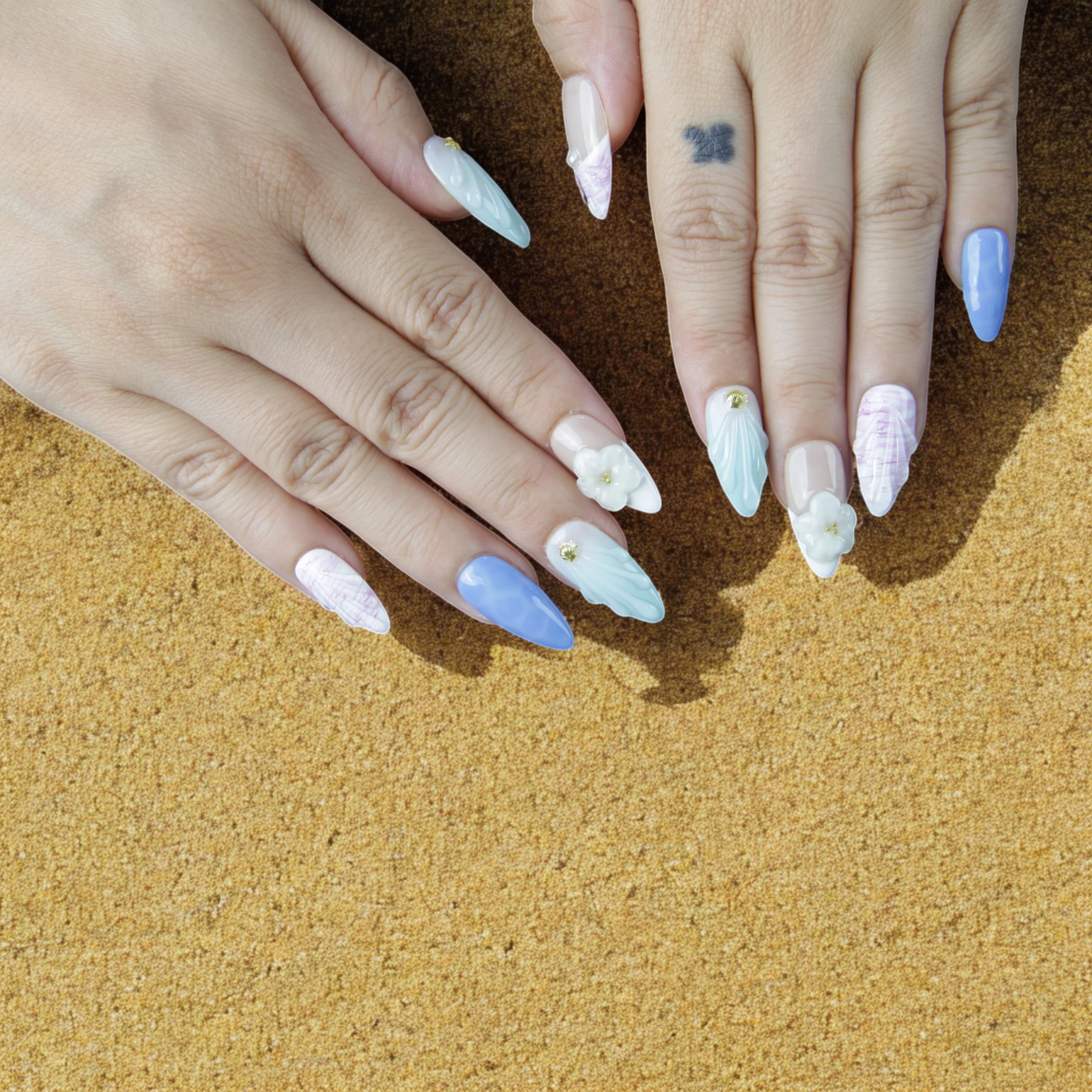 Hand model showcasing Mystic Ocean press on nails with a mix of blue, white, and nude tones, detailed with pearls and gold embellishments.