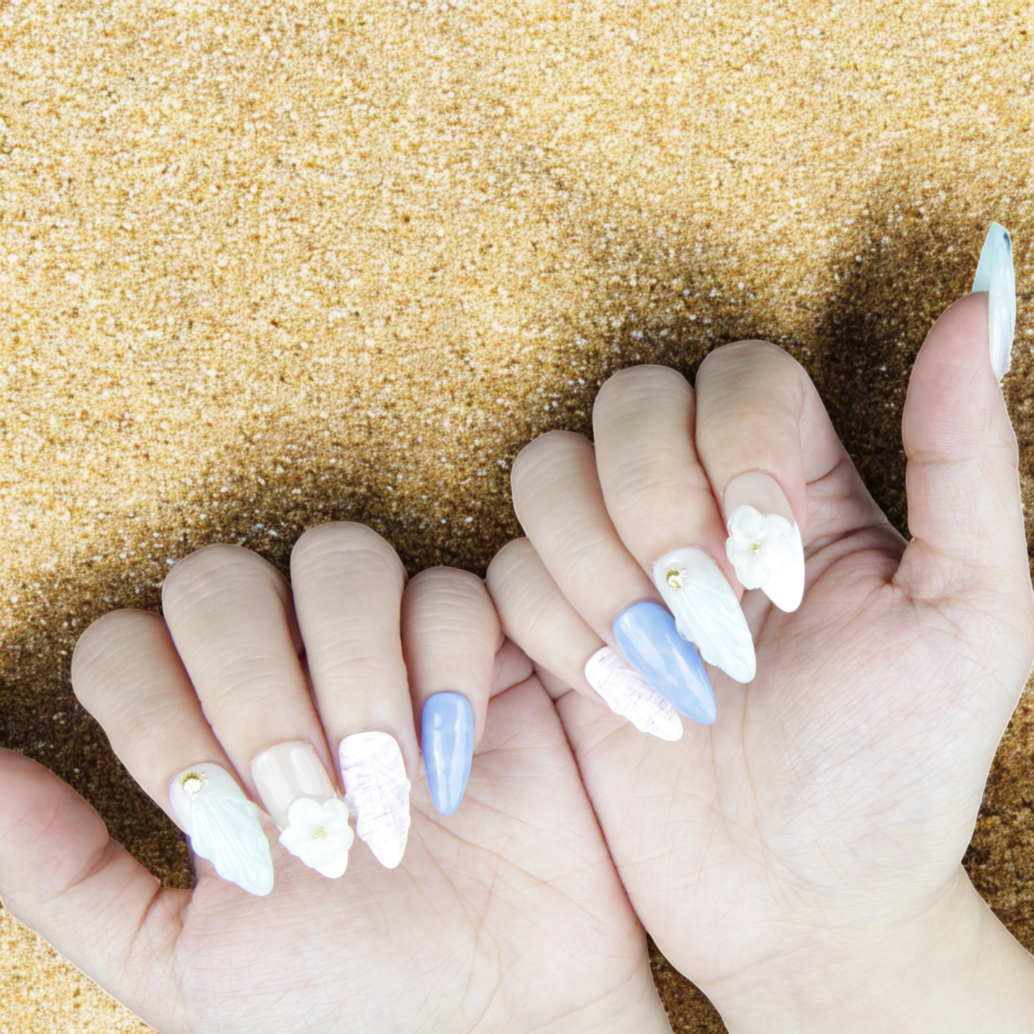 Aesthetic hand pose with Mystic Ocean press on nails, surrounded by shells and natural sand for a beachy, elegant look