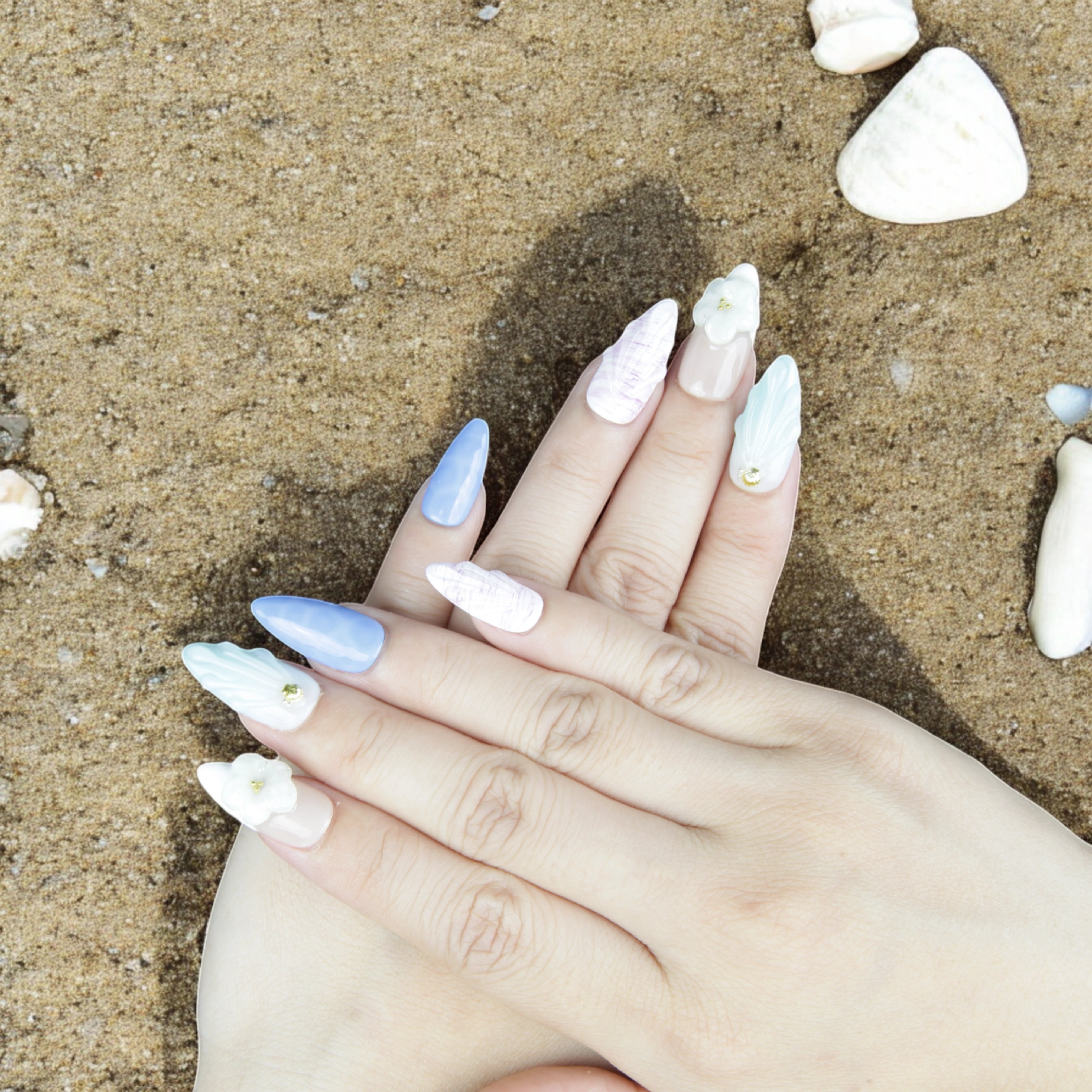 Fashionable hand pose wearing Mystic Ocean press on nails, featuring soft pastel hues, 3D details, and floral embellishments against a bold outfit.