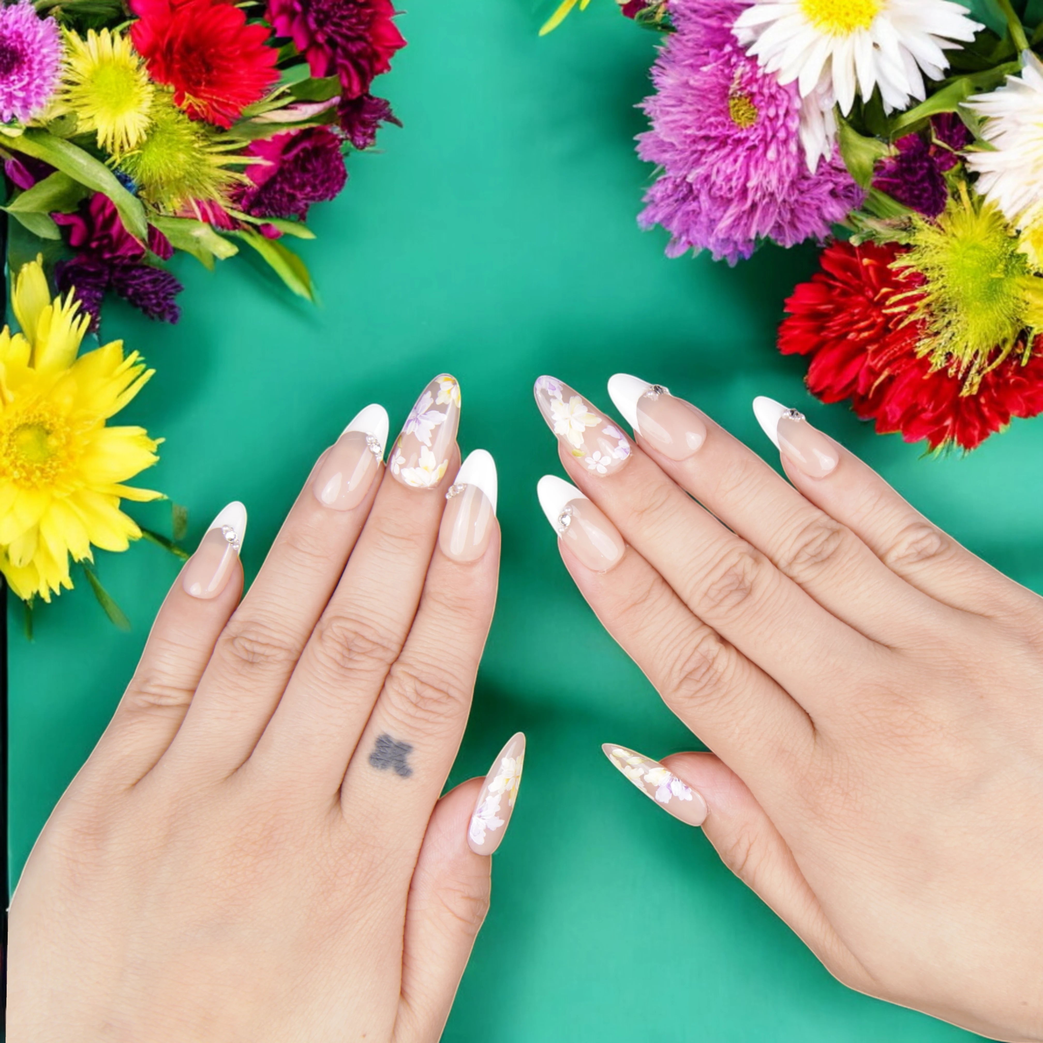 Hand-model showcasing floral French tip press on nails, styled with delicate white daisies and subtle rhinestone accents.