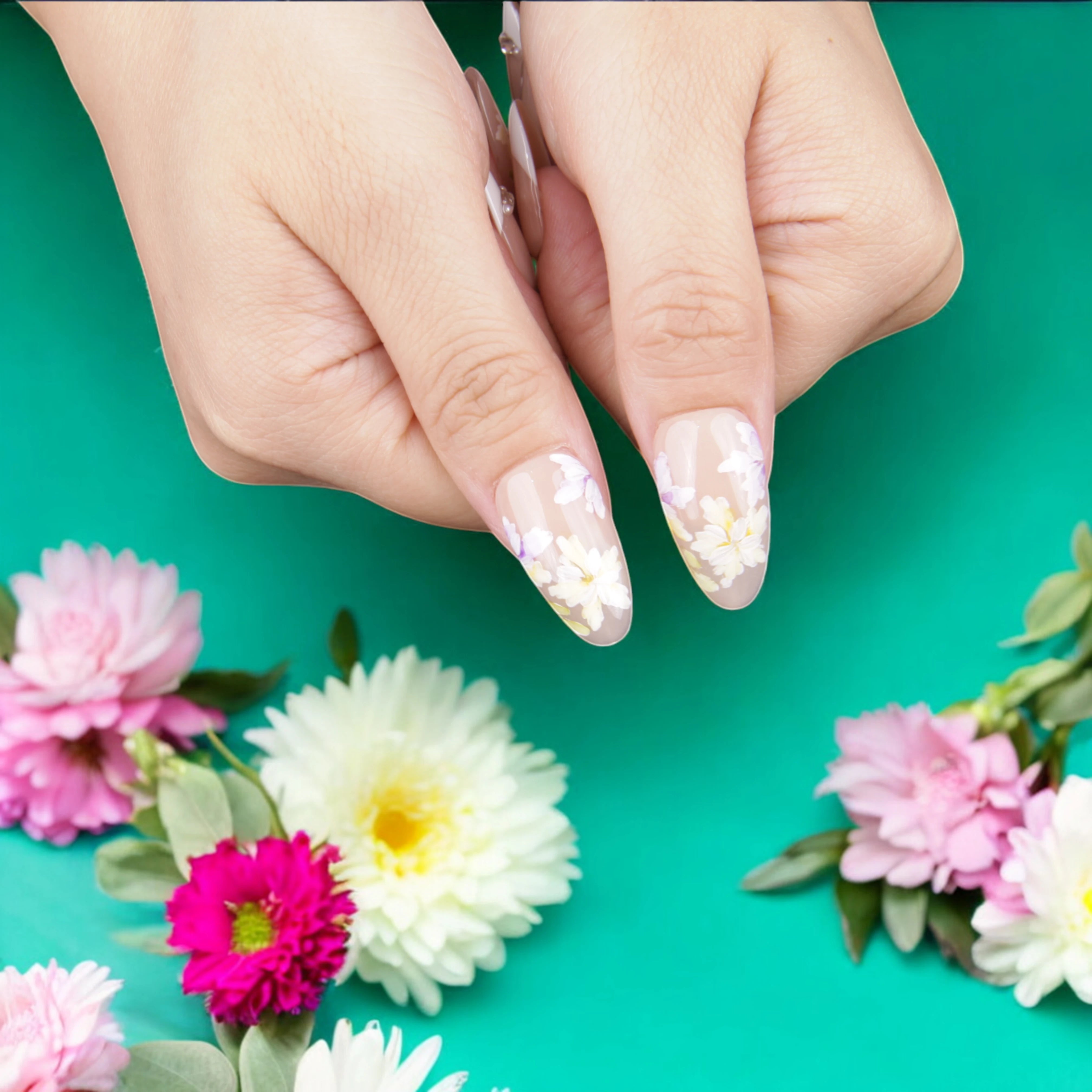 Close-up of nude and white press on nails with detailed daisy patterns and shimmering embellishments for a timeless, elegant look.