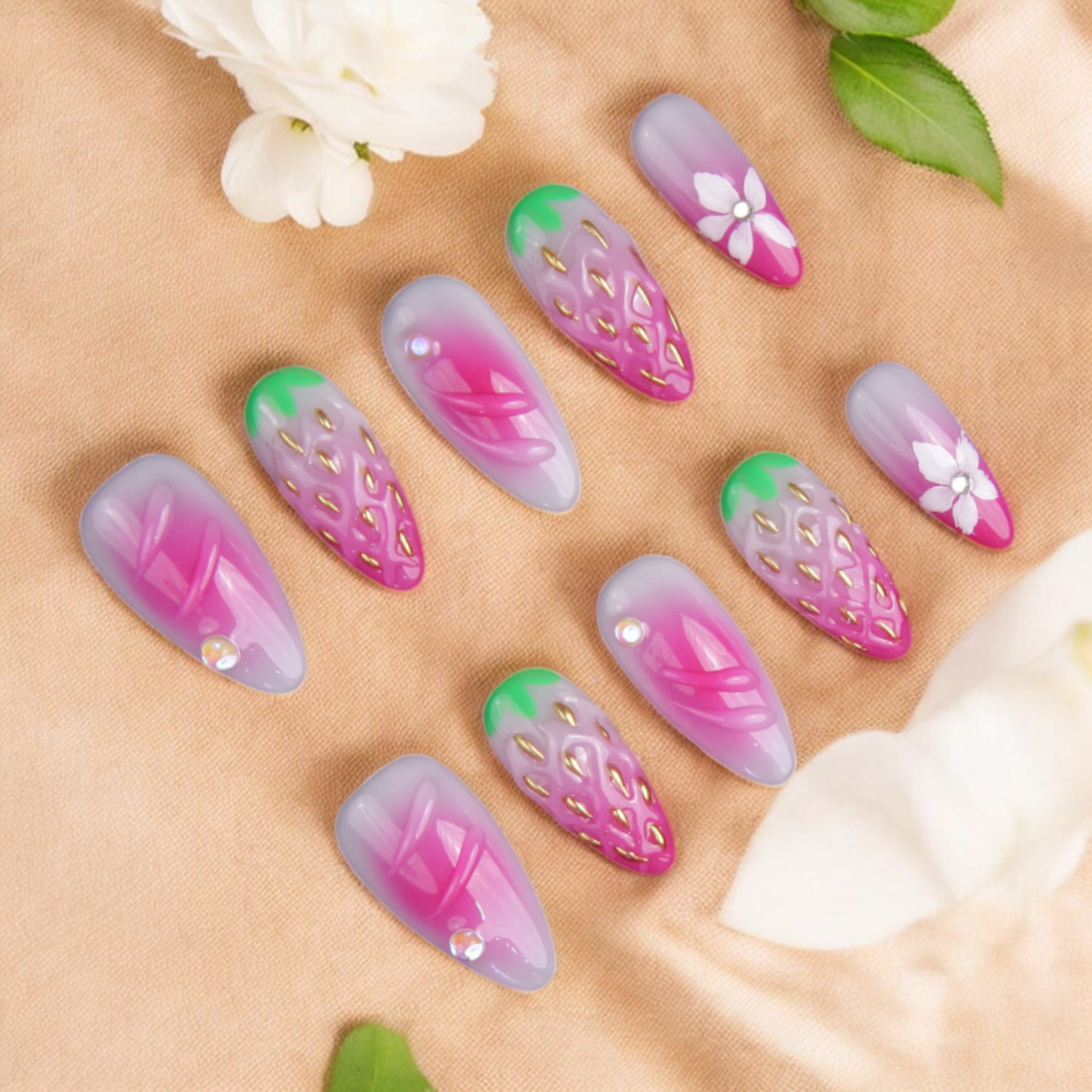 Strawberry-themed false nails with intricate 3D details, gold-seed accents, and hand-painted floral designs on a soft ombre pink base