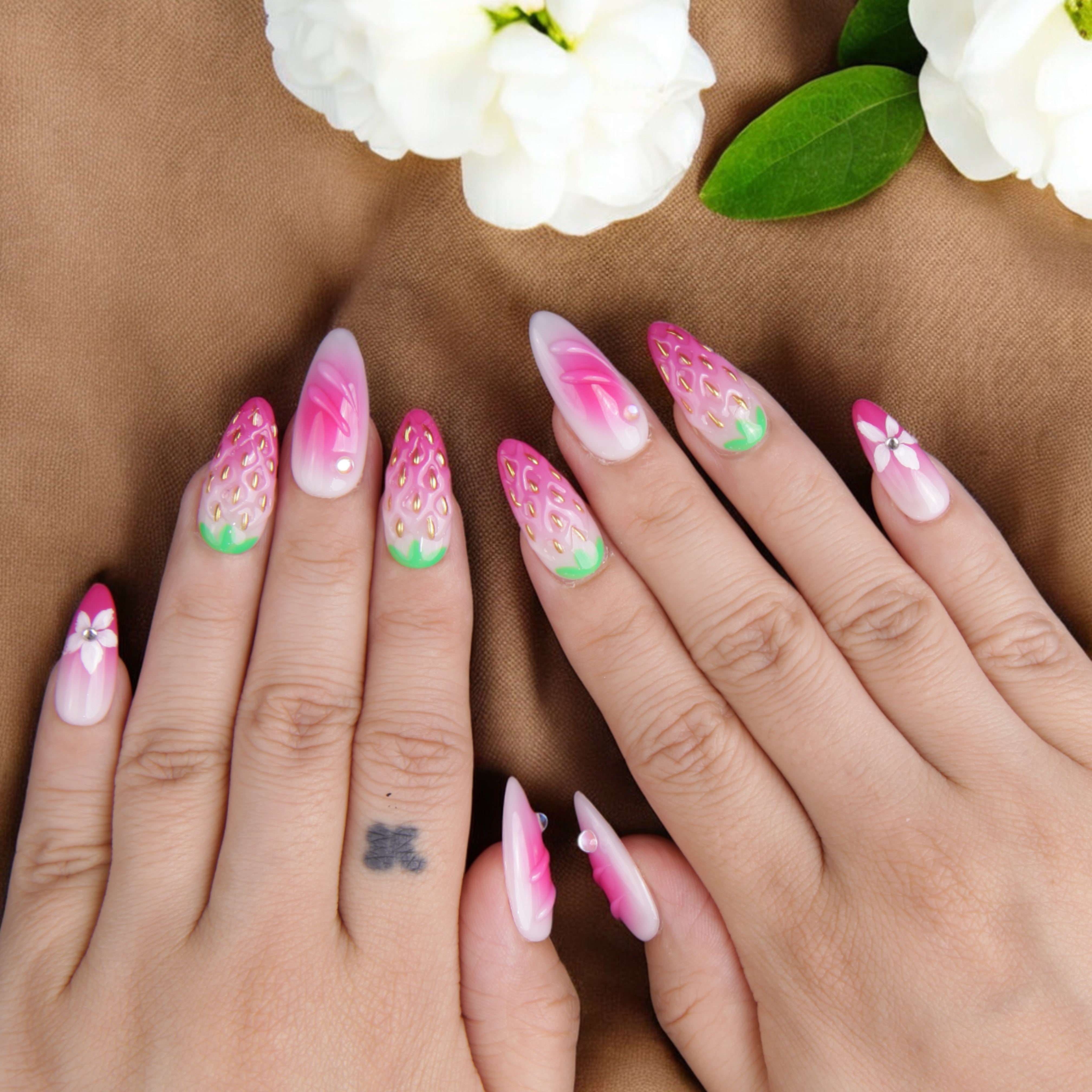 Hand model showcasing vibrant strawberry-inspired fake nails, featuring realistic texture, floral accents, and glossy finish for a fresh summer look