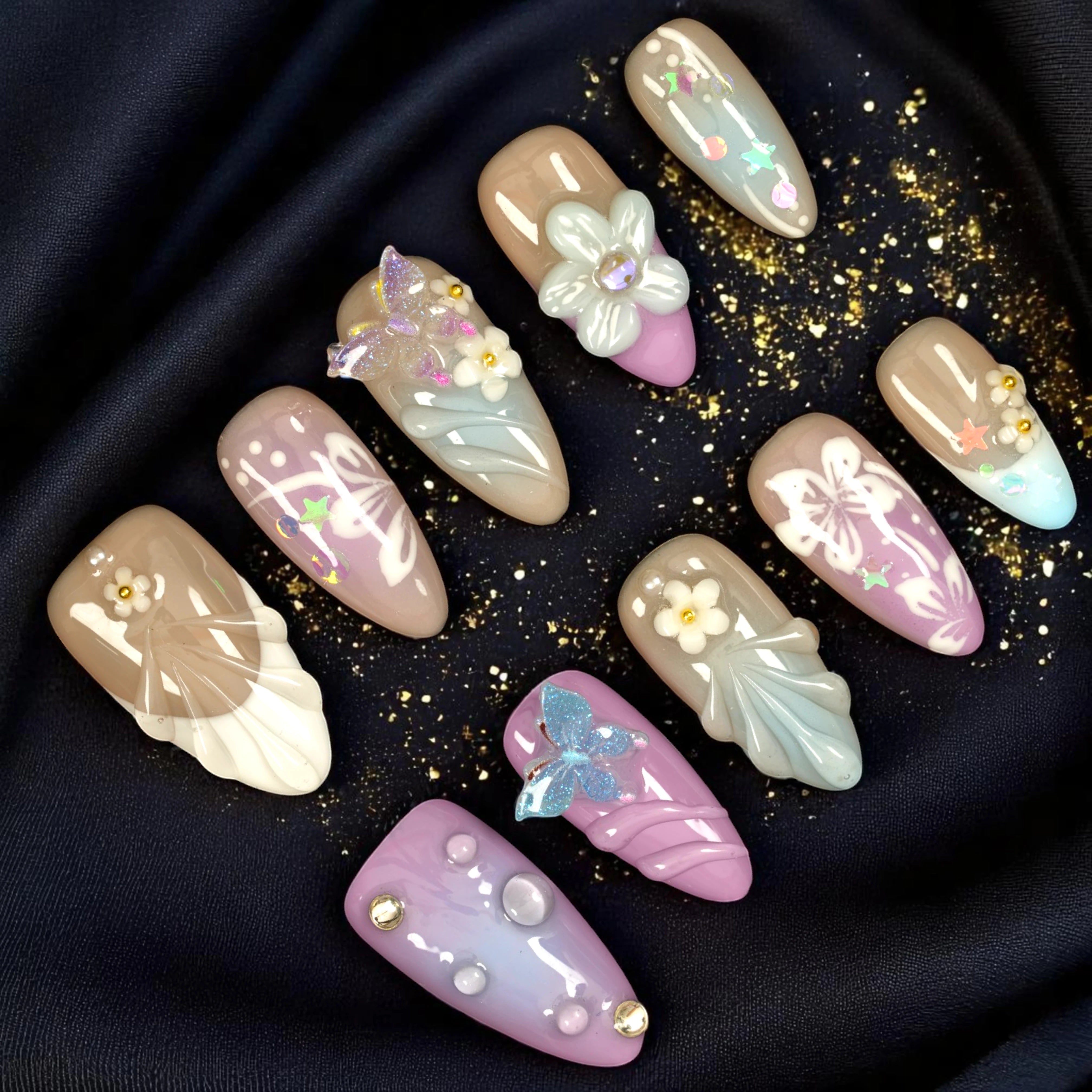 Handmade press on nails set featuring neutral tones, pastel butterflies, floral 3D accents, and pearl details on a black silk background. Perfect false nails Australia
