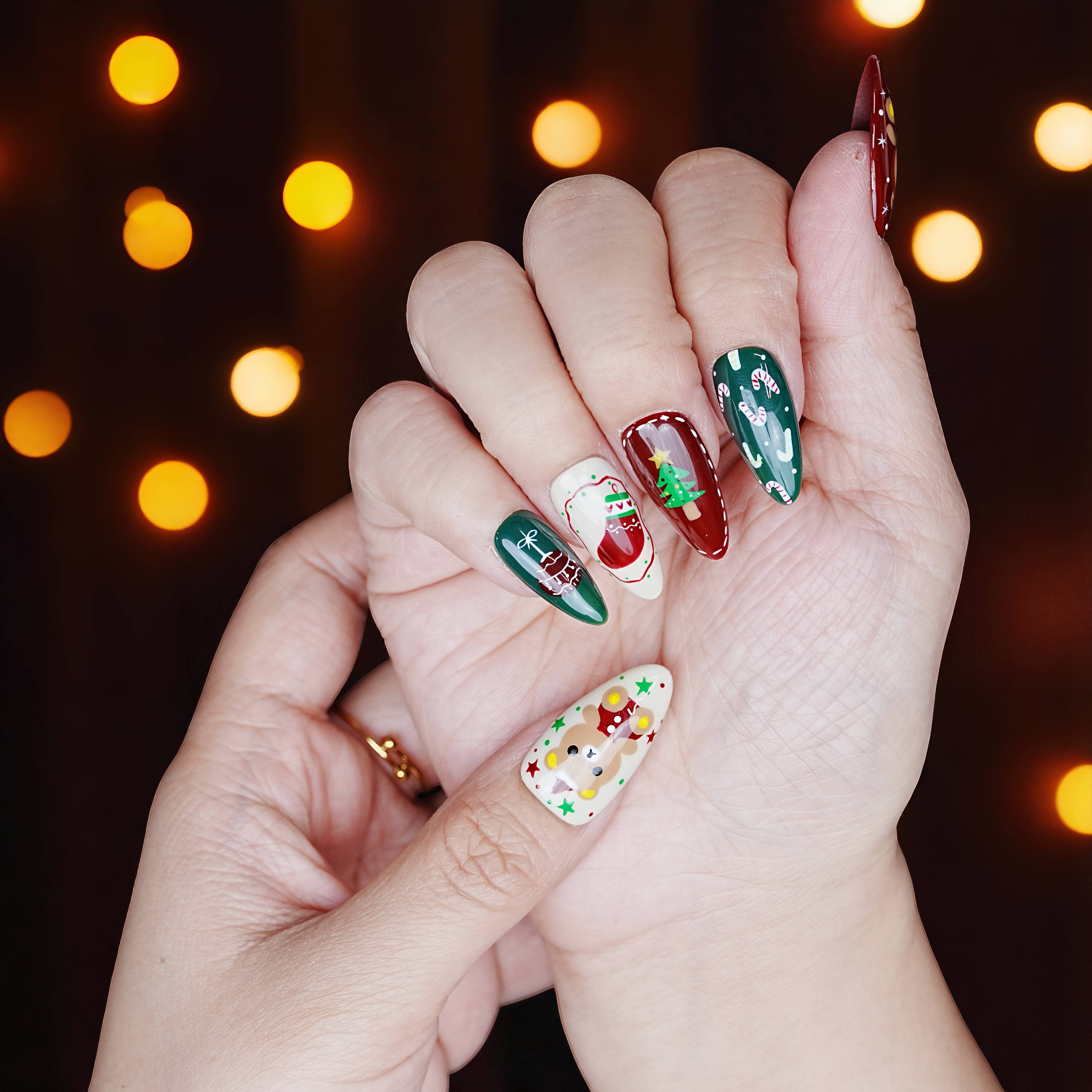 Hand pose with Christmas cookie press on nails and metallic green accents under fairy lights.