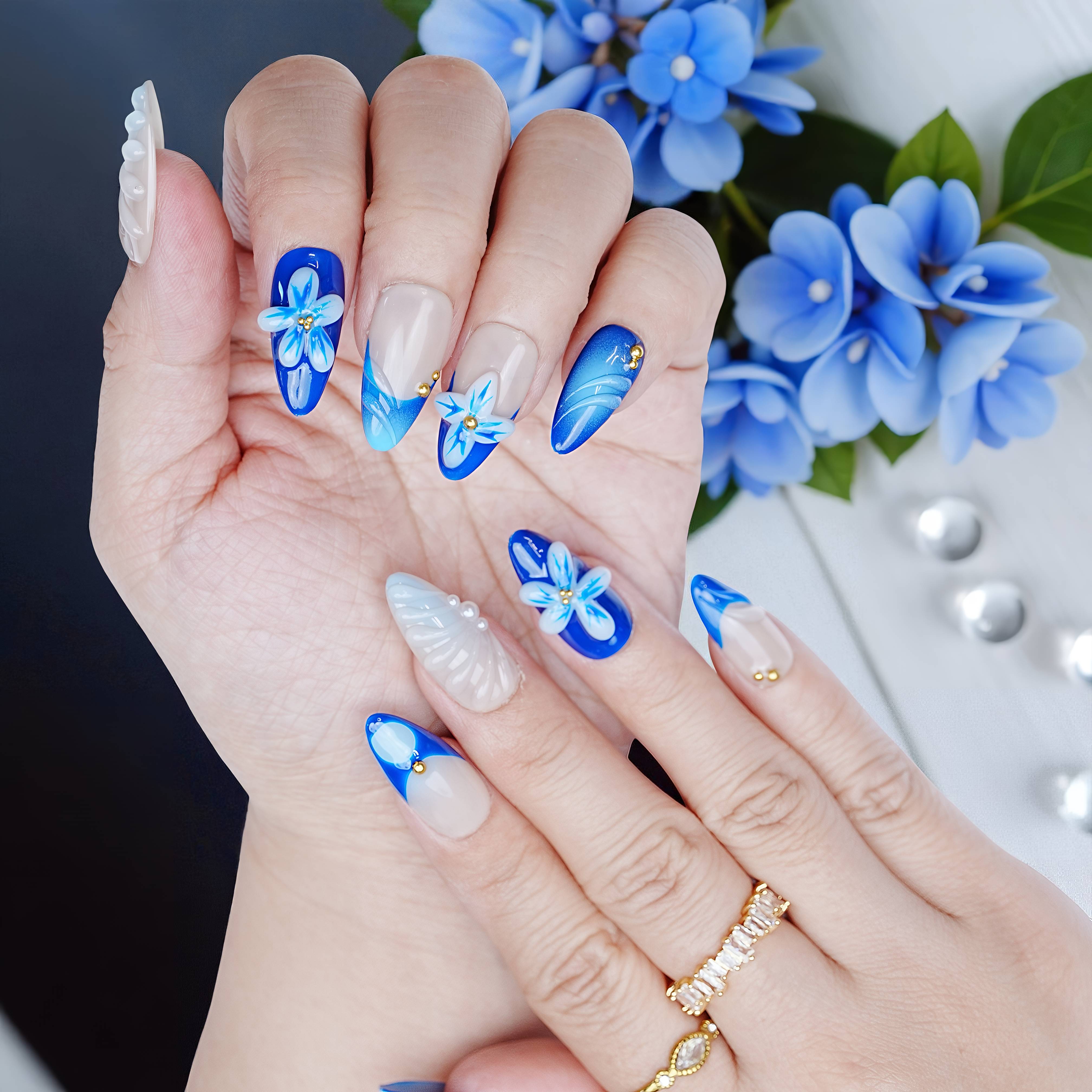 Nails shown with floral accent fingers and blue petal-inspired tips against a backdrop of blue flowers.