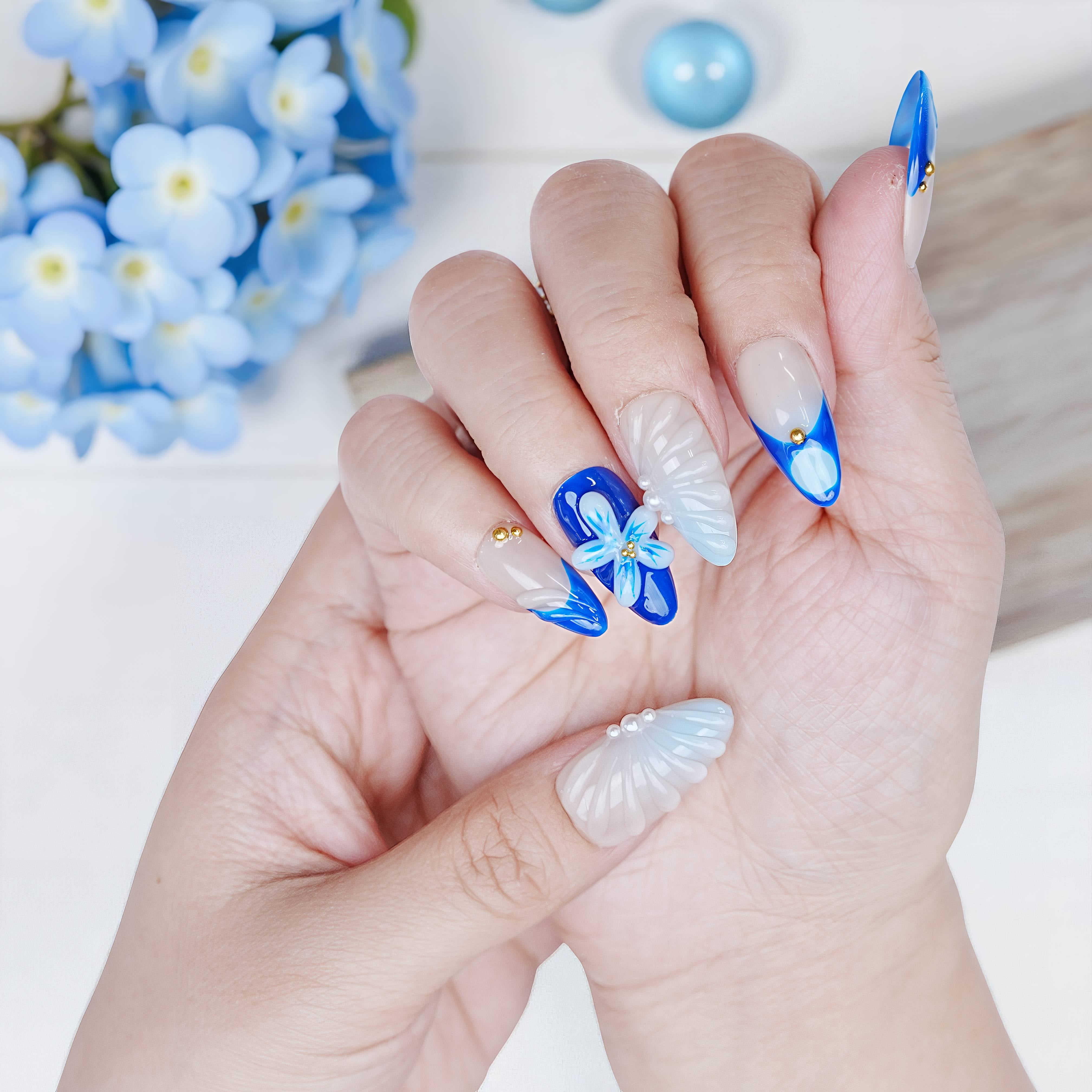Close-up of Blue Mirage nails with bright blue flower design and 3D shimmer texture, styled with soft blue props.