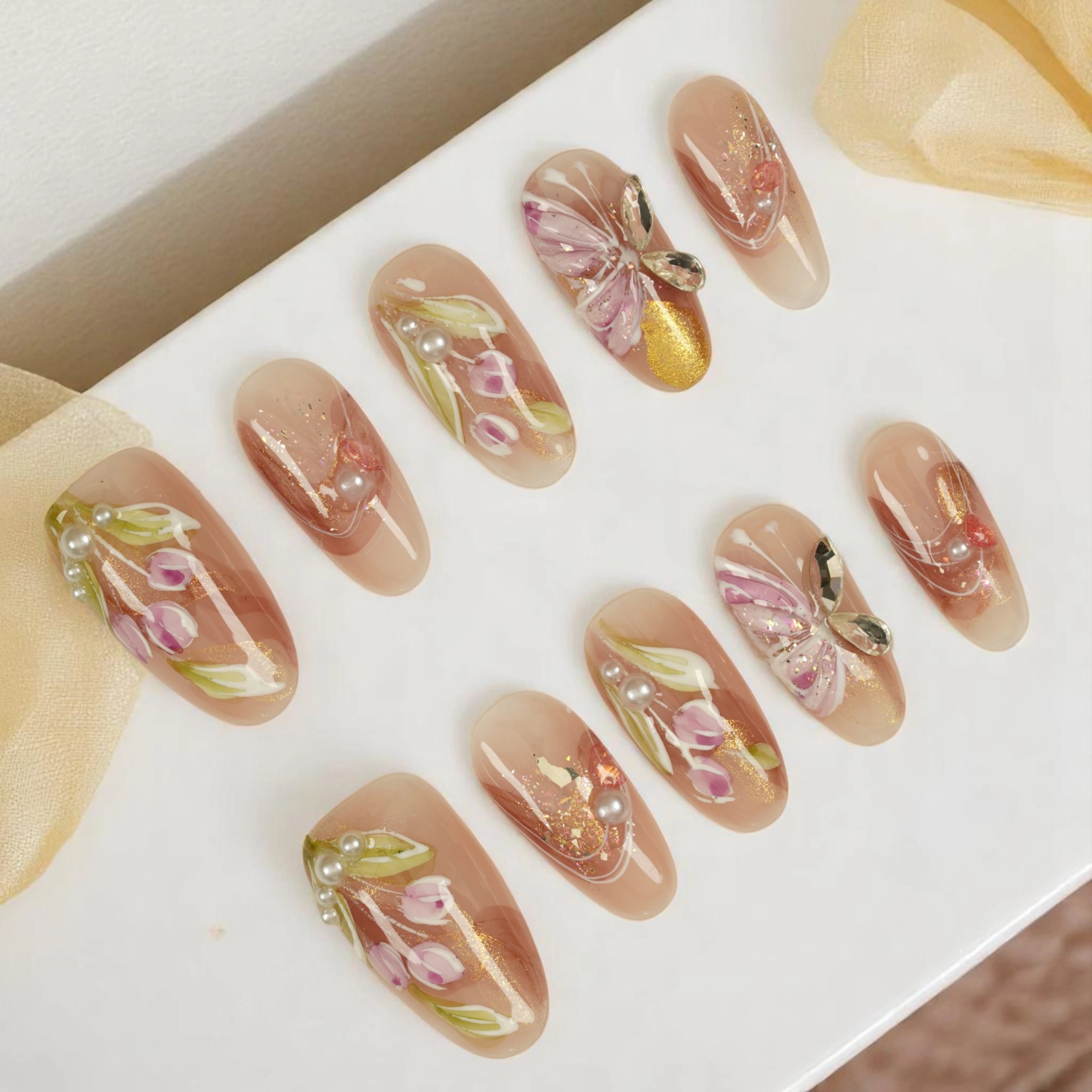 Flat lay of floral butterfly press on nail set, featuring 3D flowers, pearls and shimmer gold details — reusable handmade false nails Australia