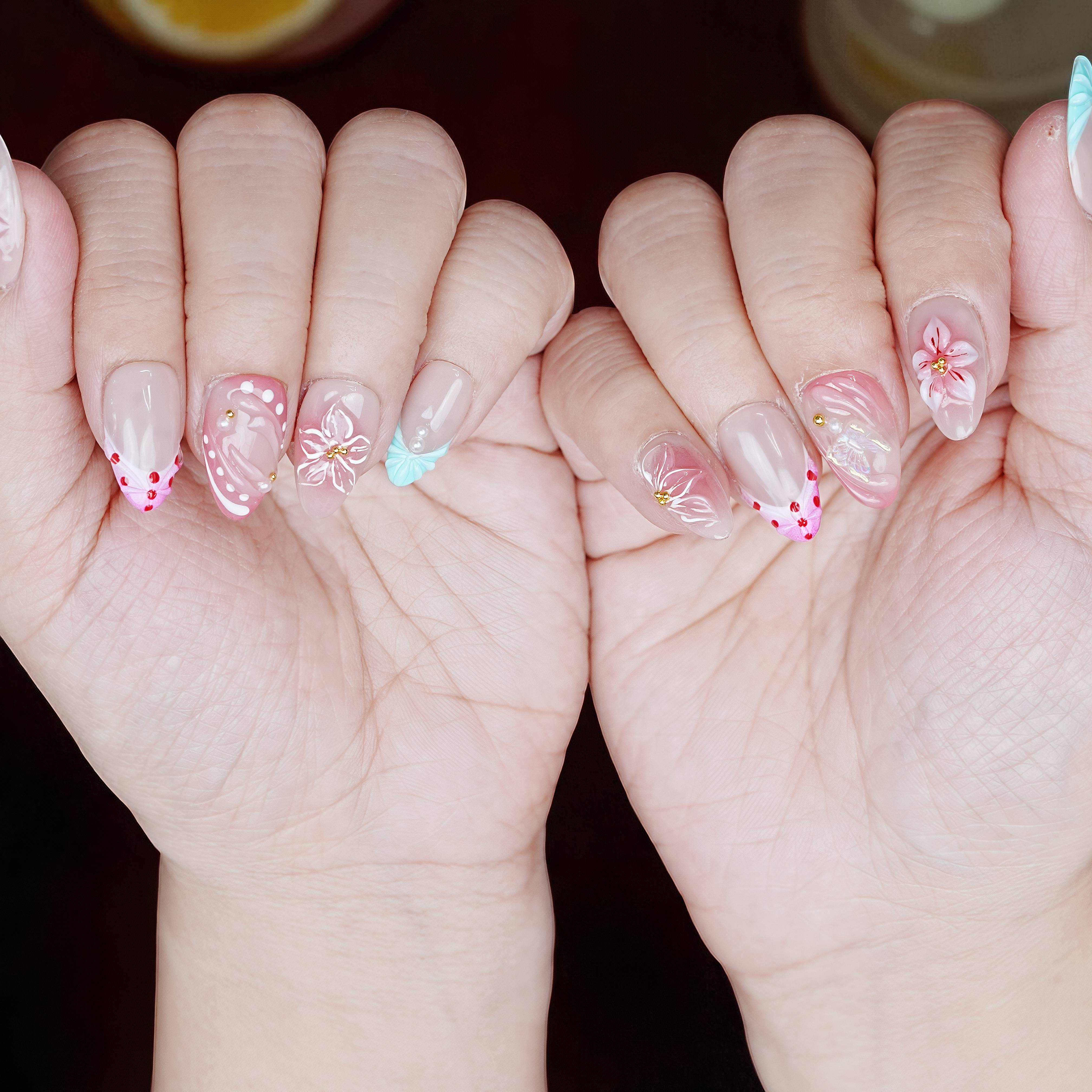 Even lighting showing soft pastel pink nails with 3D flowers, mint leaf accent, and dotted hearts.