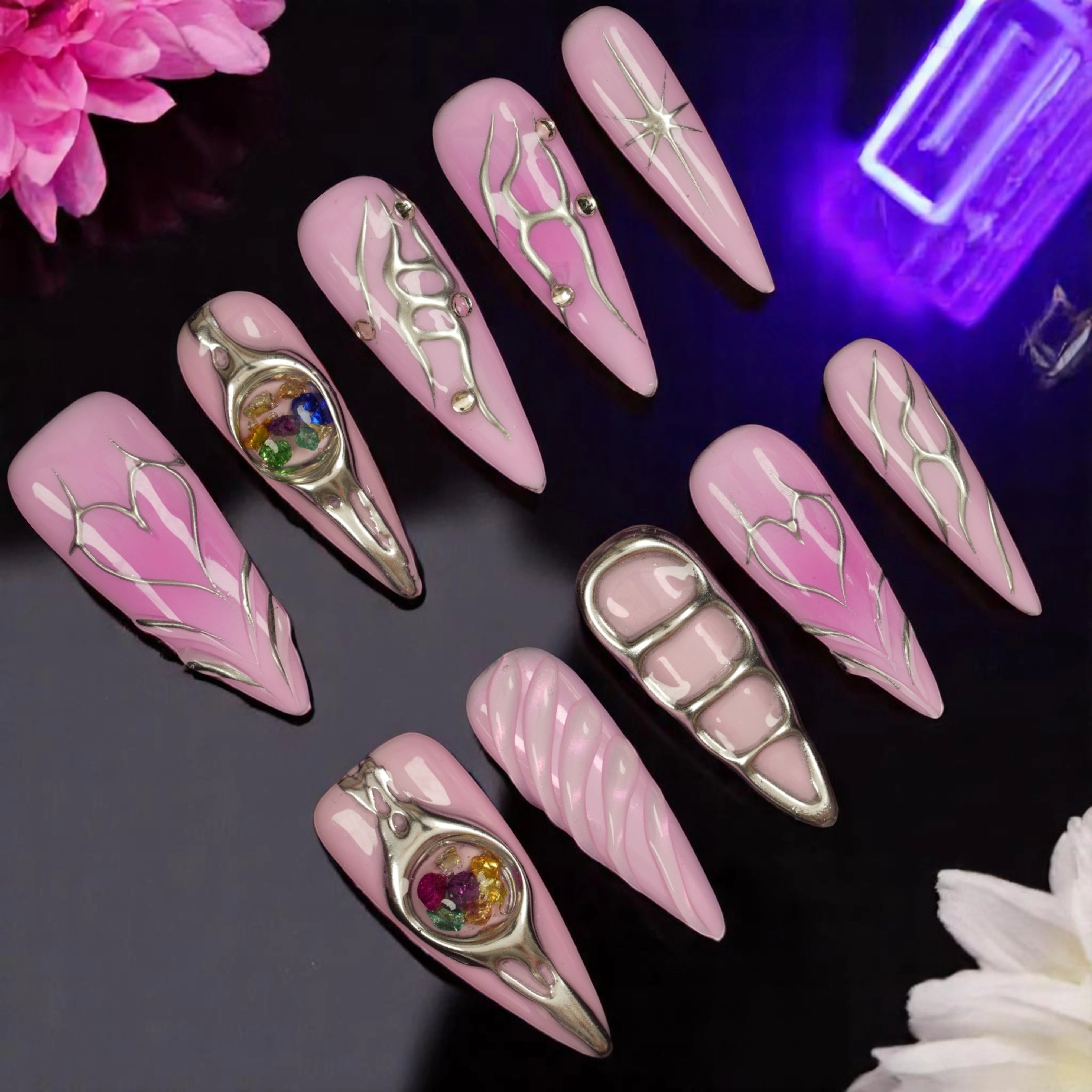 Flat lay of pink stiletto press on nails with chrome line art, 3D cosmic gemstone spheres, and sculpted heart accents