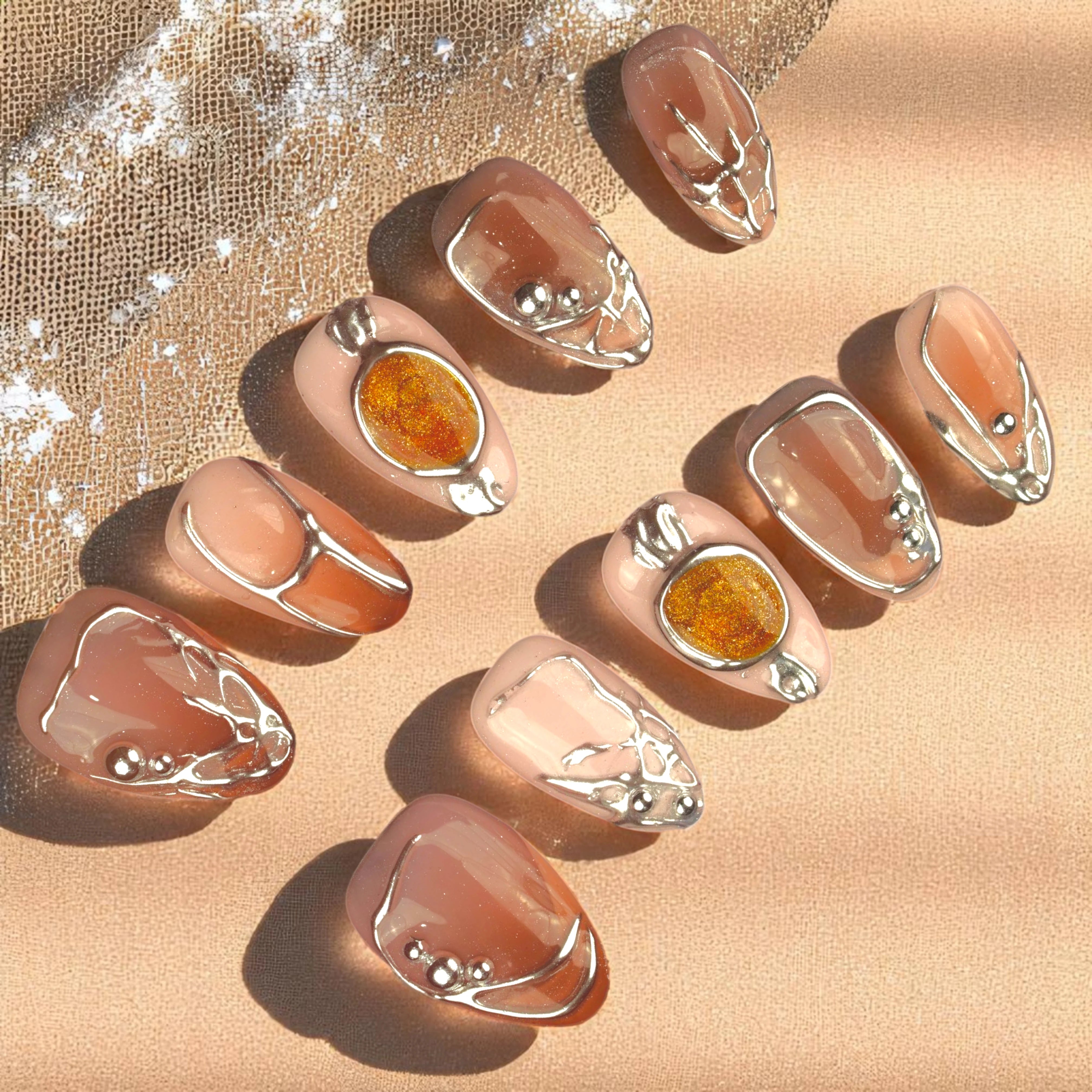 Flat lay of nude press on nails with silver metal frame accents and amber stone embellishments on a soft neutral background