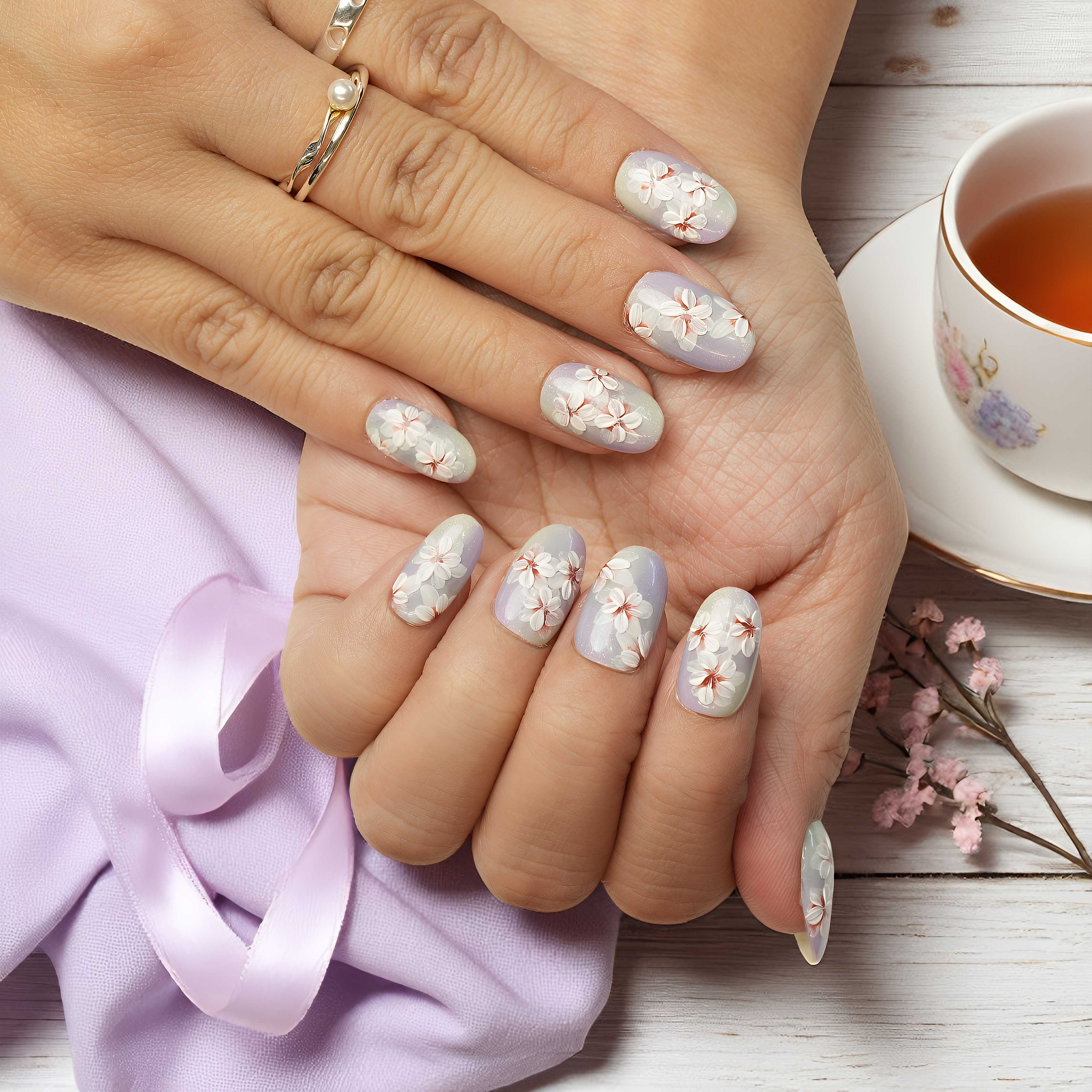 Hand with floral nail design holding a cup of tea on a wooden surface