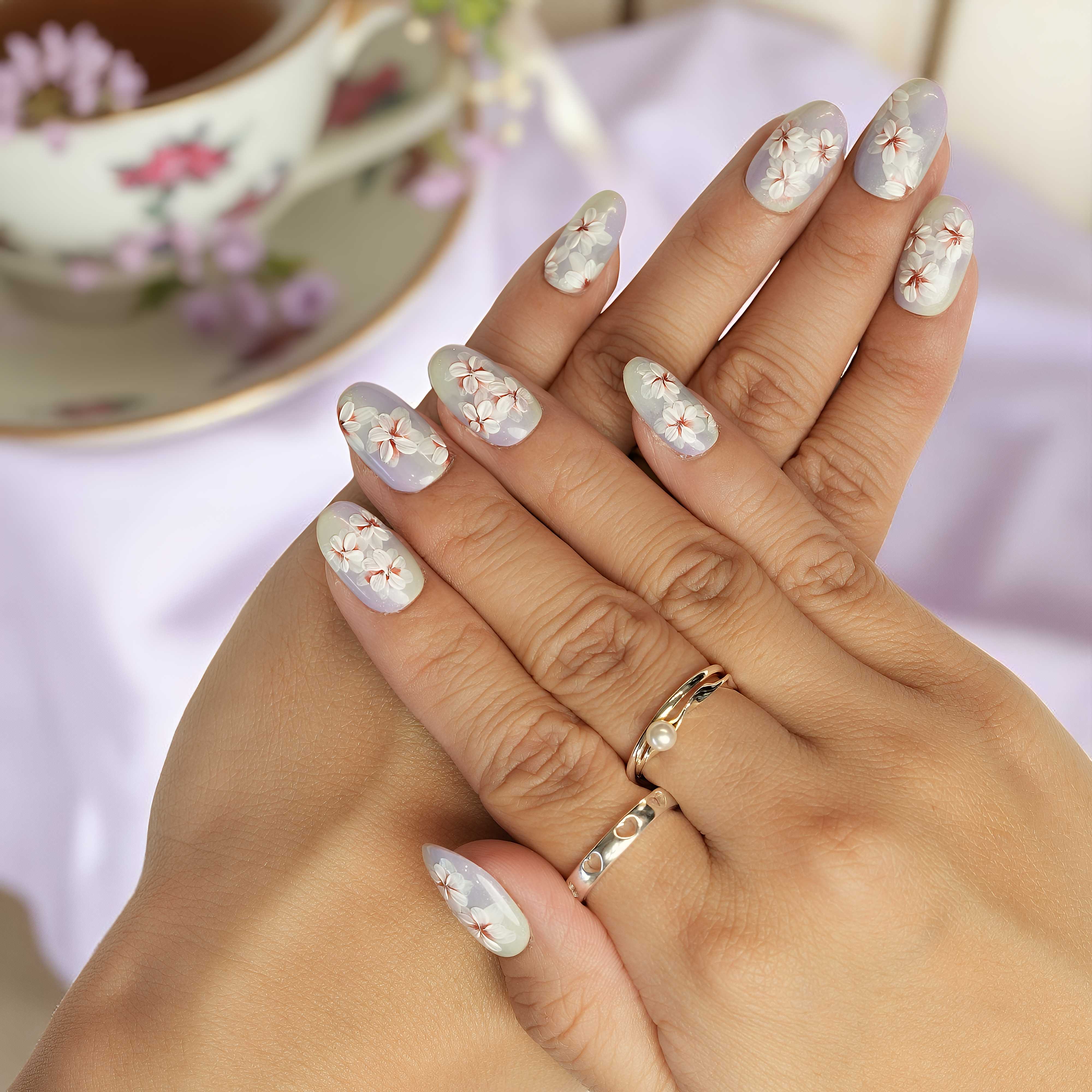 Hand with floral nail design holding a teacup with floral pattern