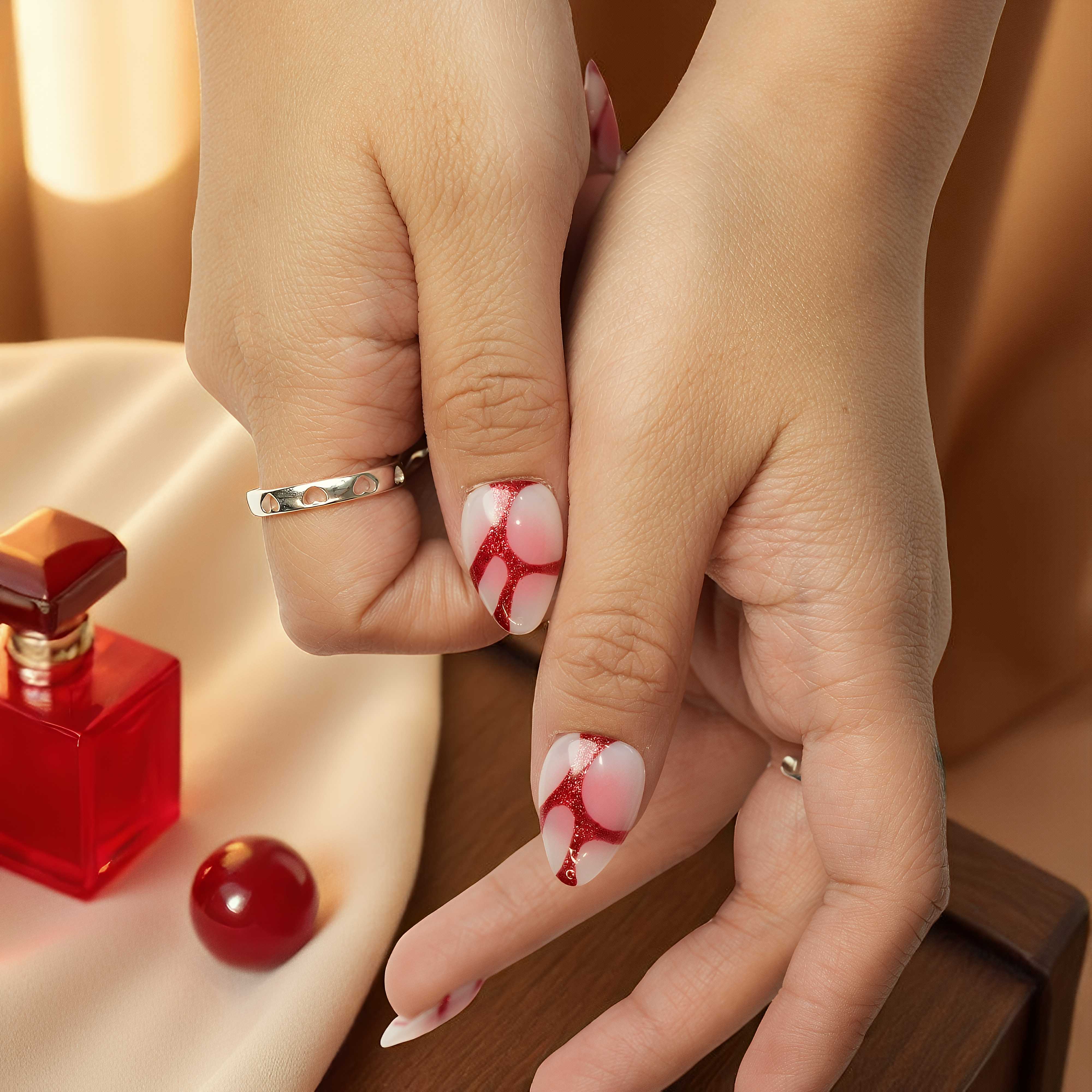 Detailed view of glue on nails near red perfume bottle, pink base with glossy red glitter abstract lines, reusable nail set in Australia.