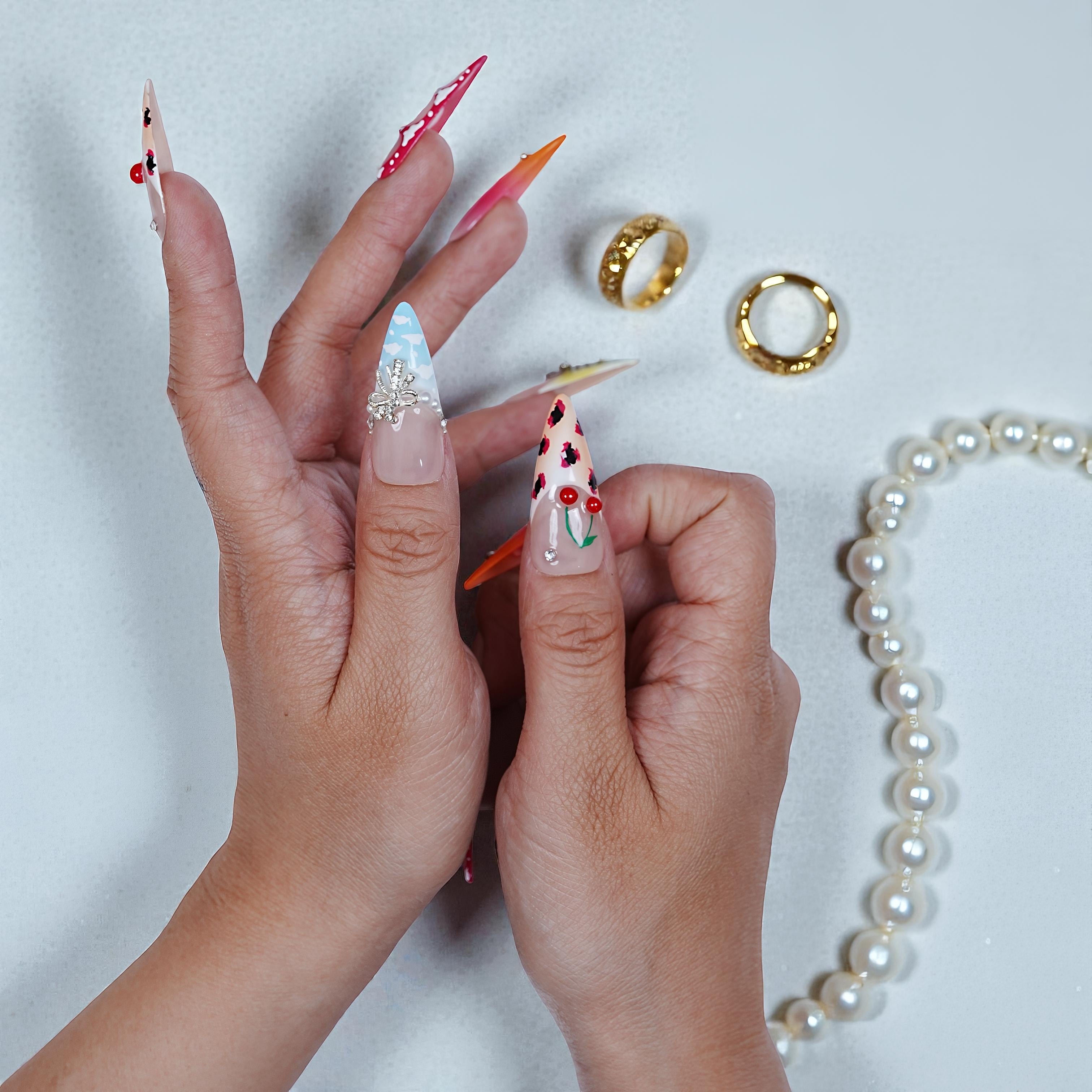 Close-up of hands with long, intricately designed nails on a light background.