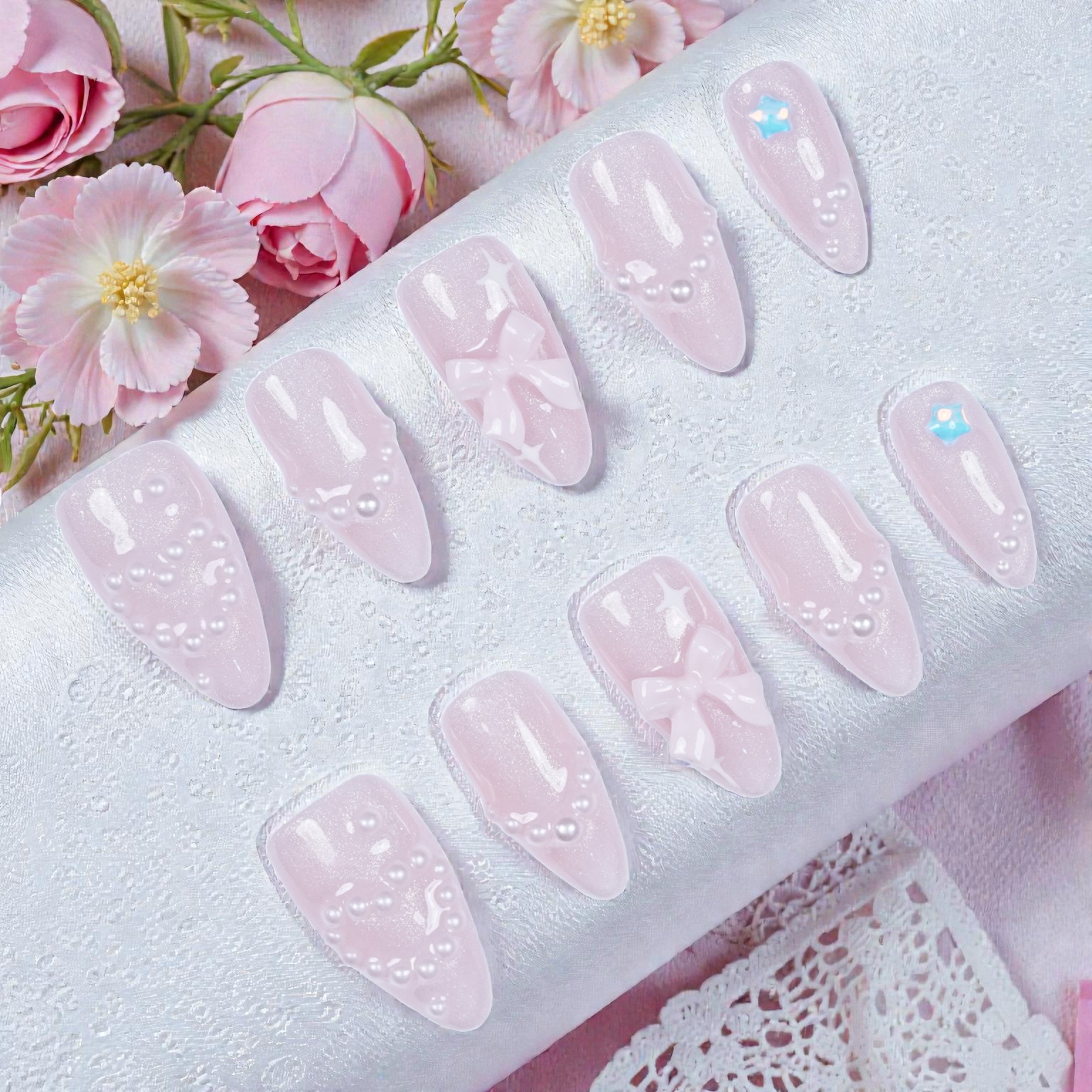Flat lay of artificial nail set showing 3D bows, floral art, and soft shimmer finish