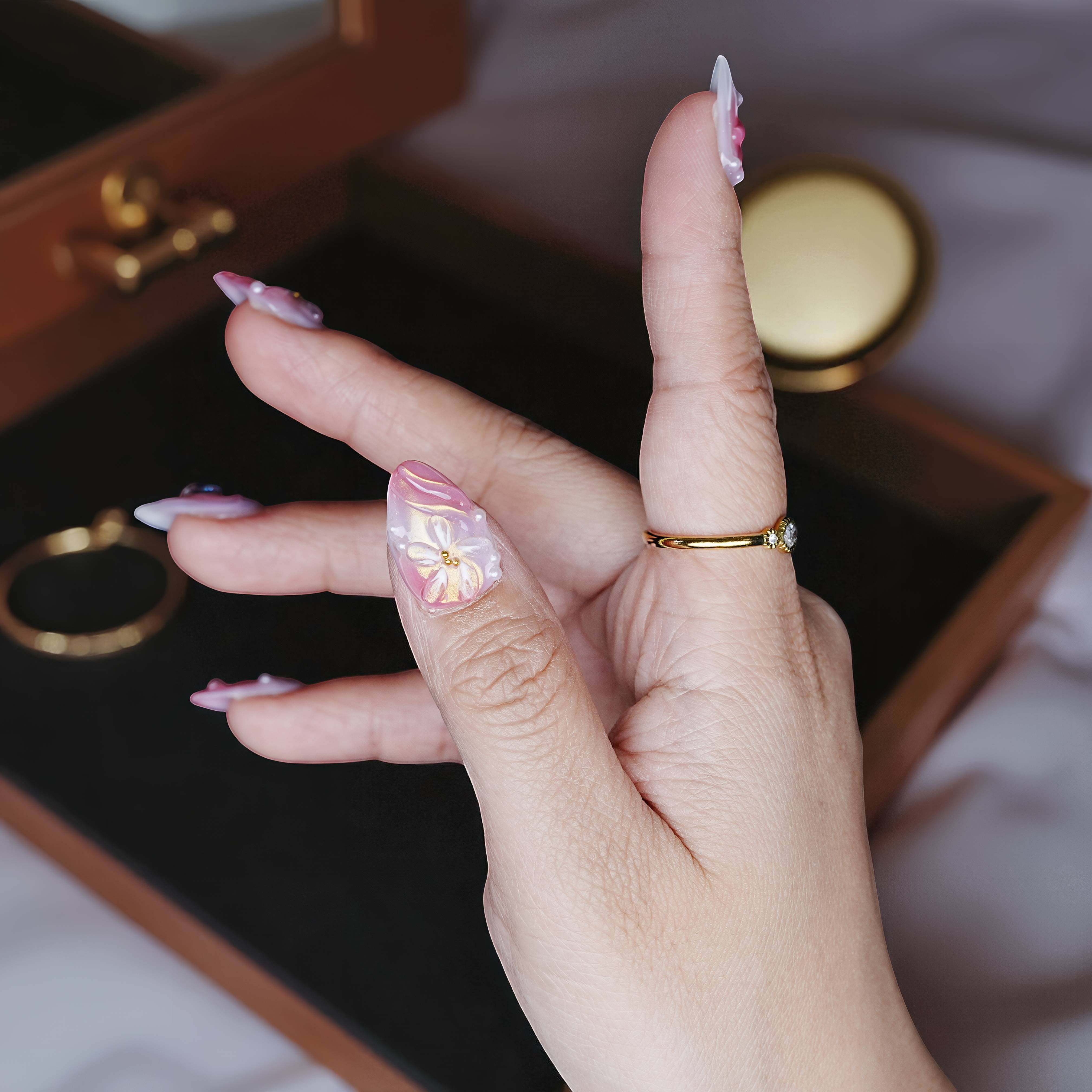 Side angle of hand showing swirl textures, 3D bows, and glossy shine in soft ombré pink.