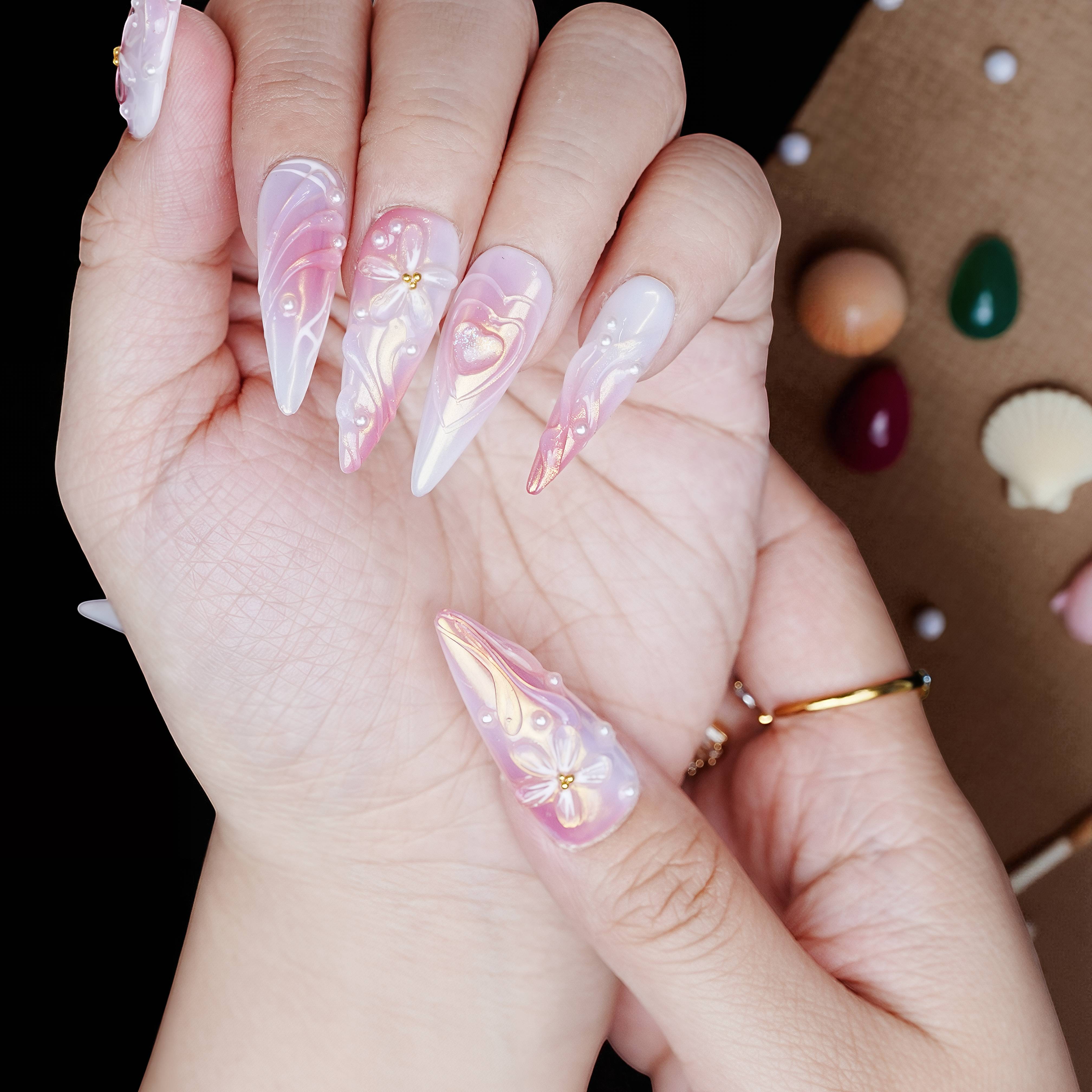 Angle view of pearlescent pink stiletto nails featuring sculpted bows, shimmer effects, and heart accents